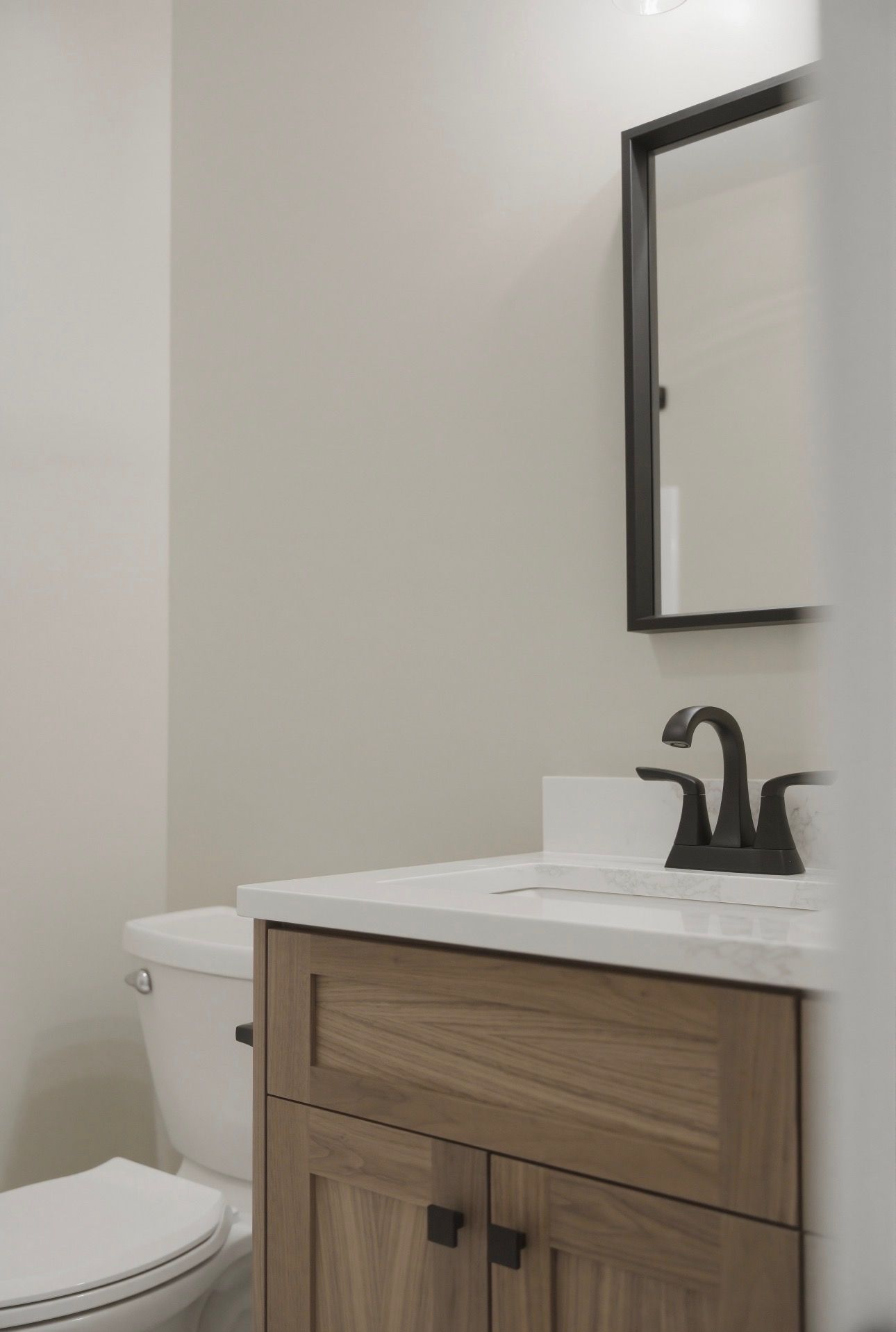 Small bathroom vanity with sink, black faucet, mirror, and white toilet against a light gray wall.