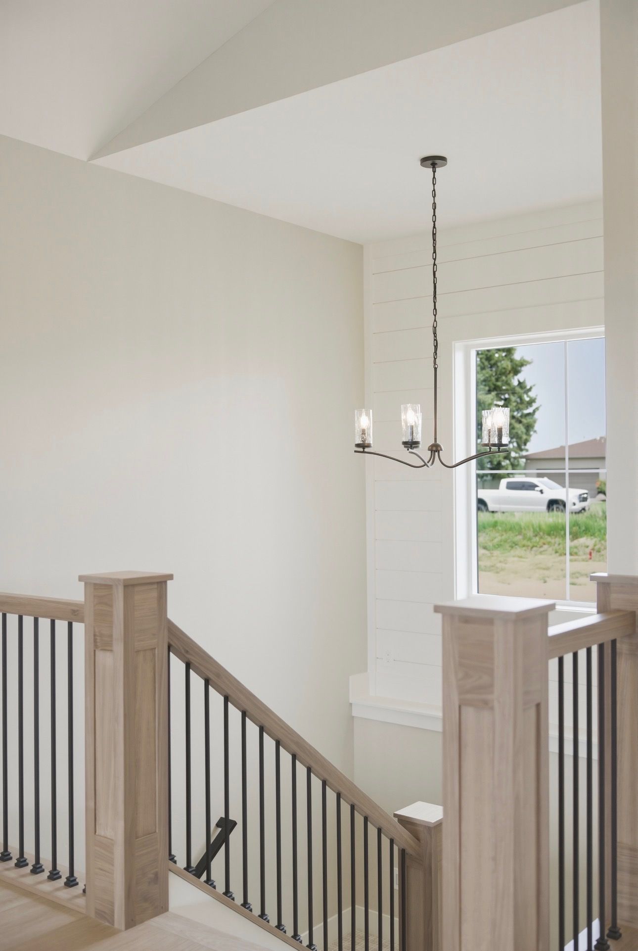 Modern stair landing with black railing, white walls, chandelier, and window view outside