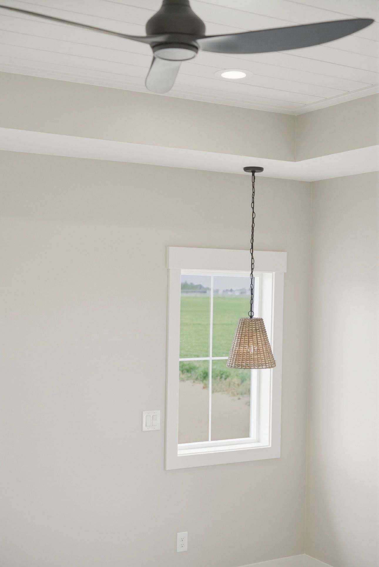 Empty beige room with ceiling fan, pendant light, and window overlooking a green field