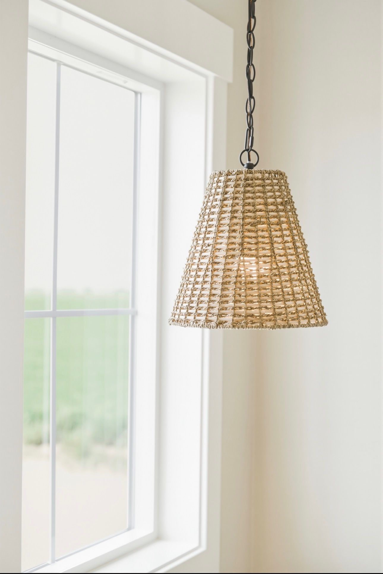 Woven pendant light hanging beside a white-framed window in a bright room