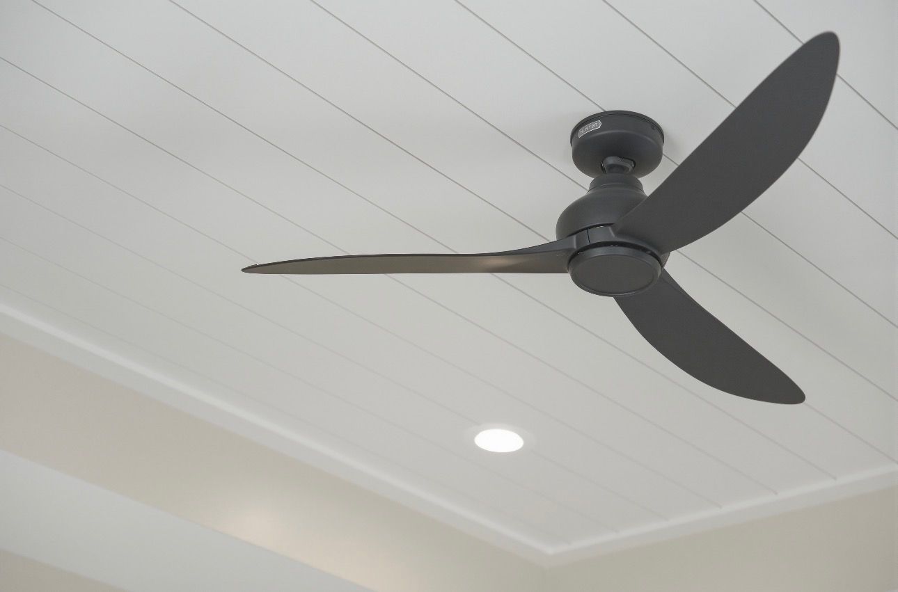 Black ceiling fan with three blades on a white paneled ceiling with a recessed light