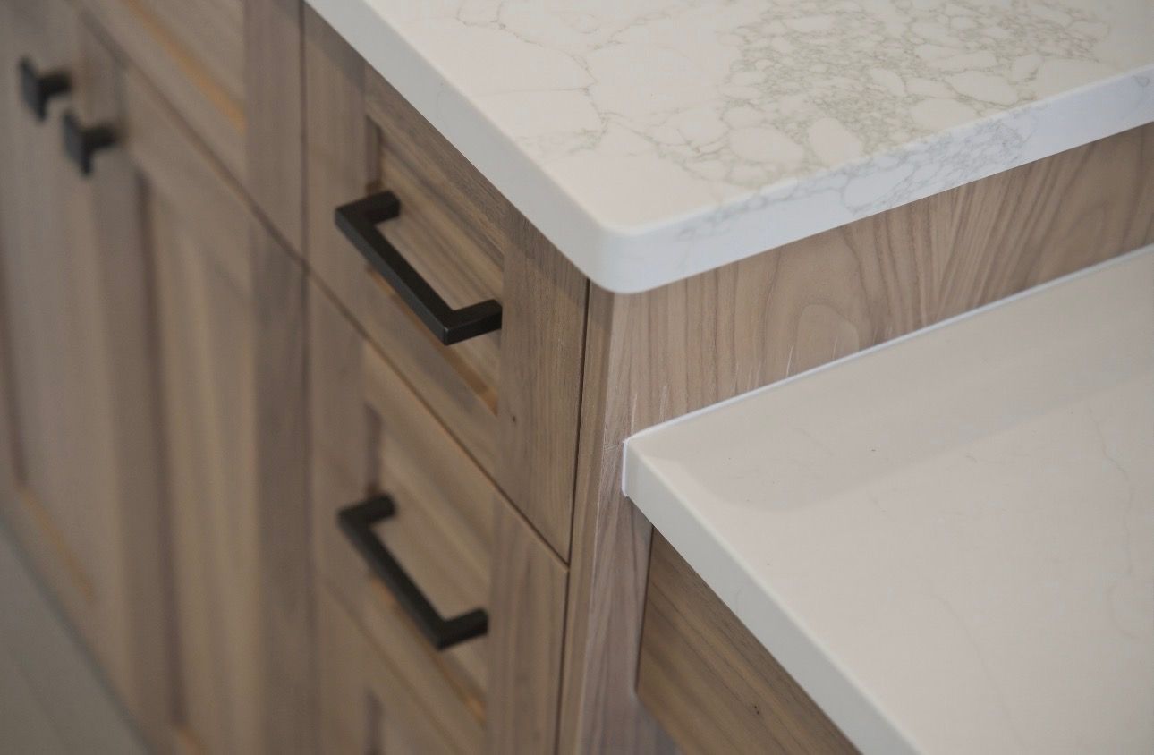 Wood cabinets with black handles beside a white countertop and island in a kitchen
