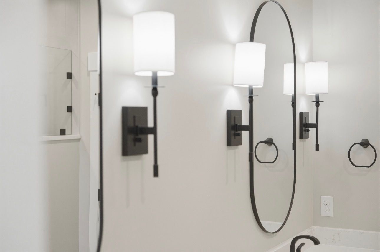 Bathroom vanity with three wall sconces, oval mirror, and white walls