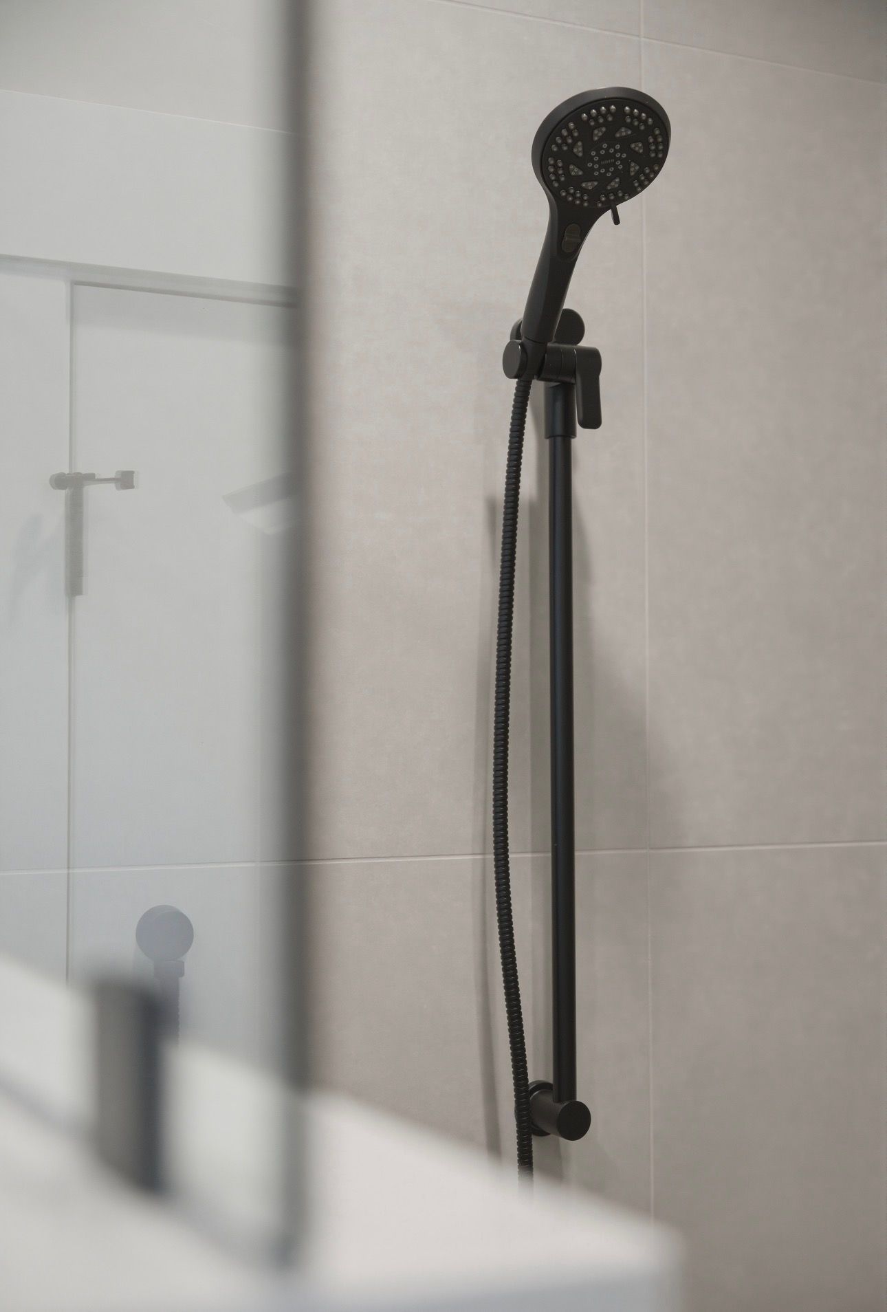 Black handheld showerhead with hose mounted on a tiled shower wall