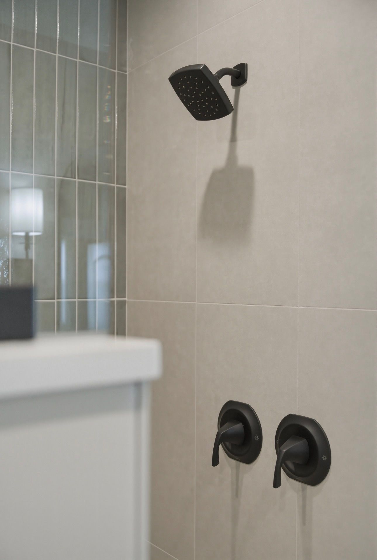 Bathroom shower with black fixtures on beige tile wall and glass partition partially visible