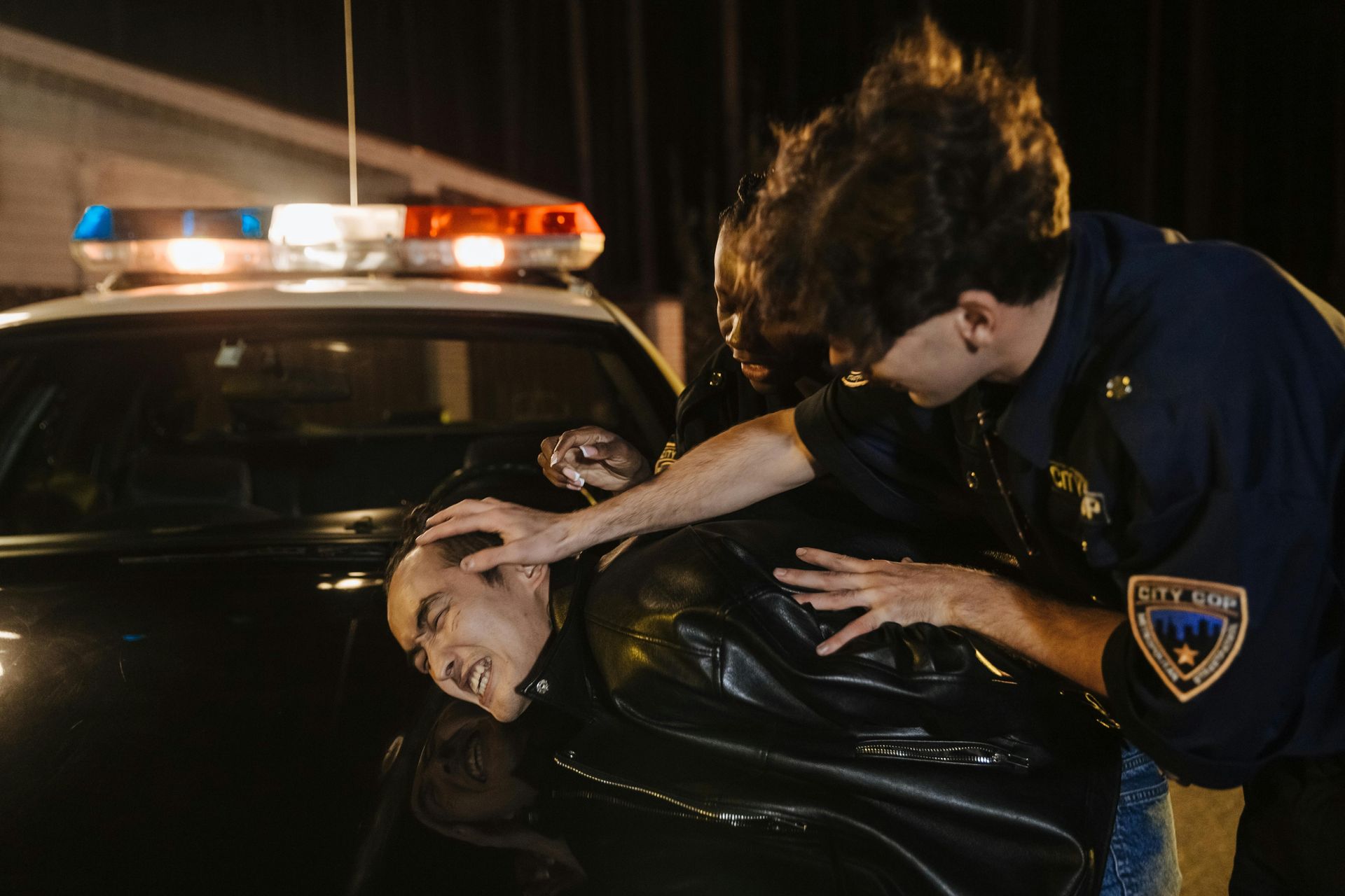 Police officers arresting a person by a squad car at night.