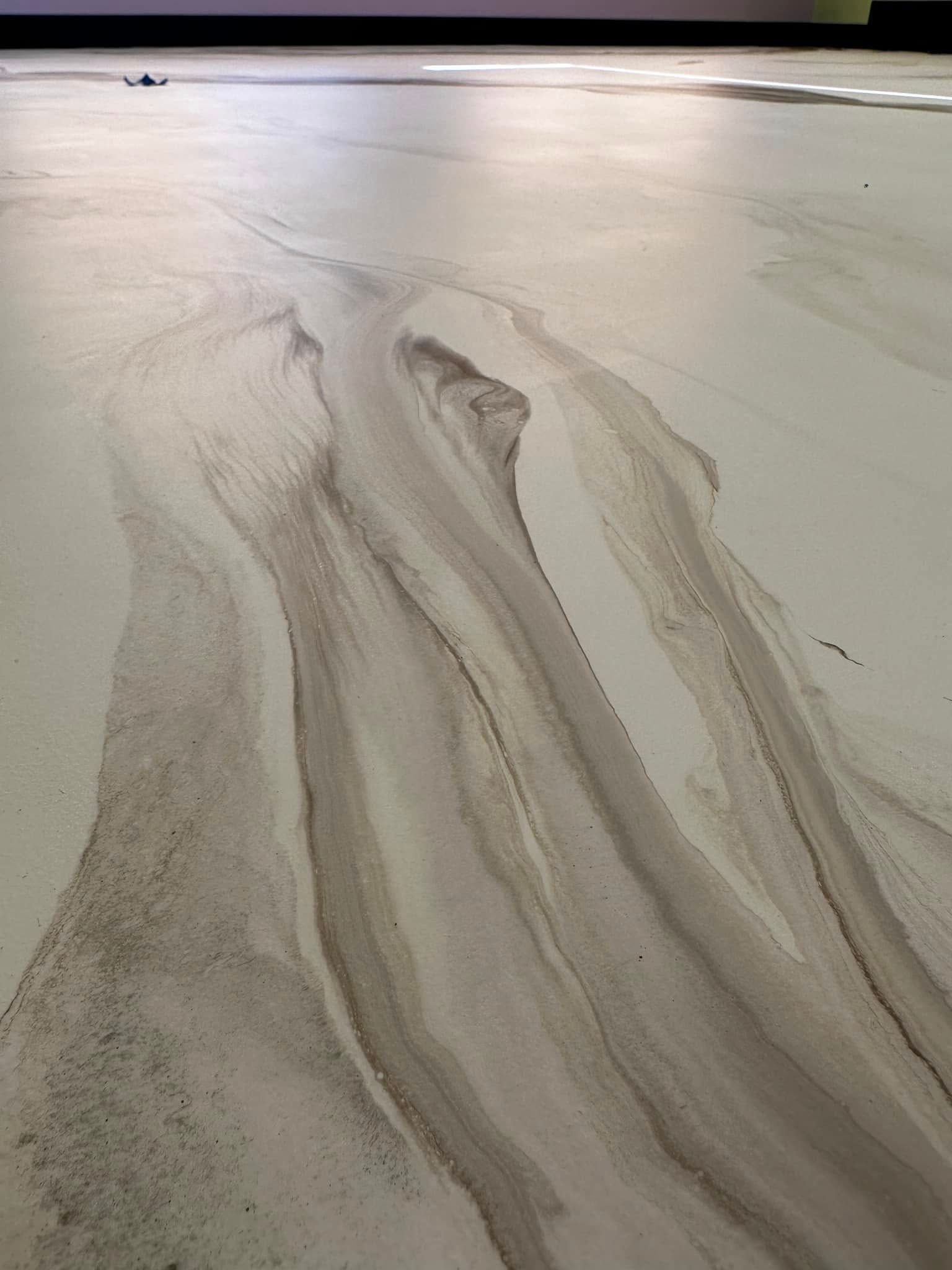 Abstract floor art: Beige and brown flowing patterns on a light background, resembling a river or trail.
