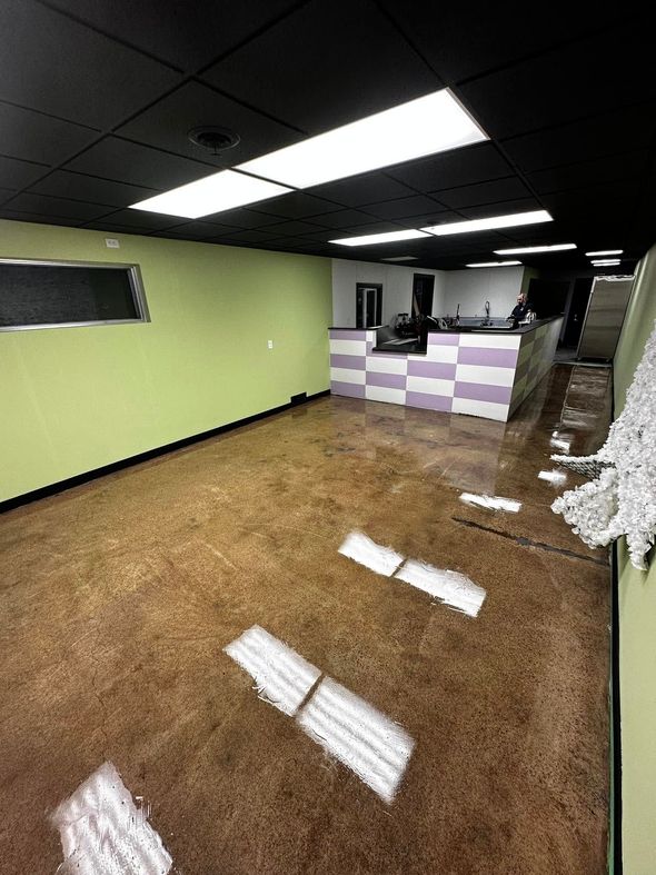 Empty retail space with brown floor, green walls, and checkered counter. Black ceiling with bright lights.