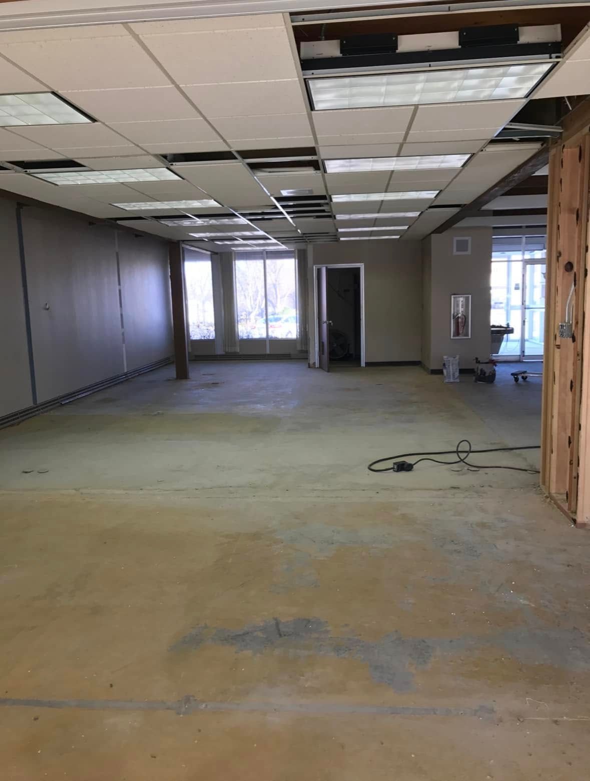 Empty commercial space with exposed ceiling, concrete floor, and windows; under construction.
