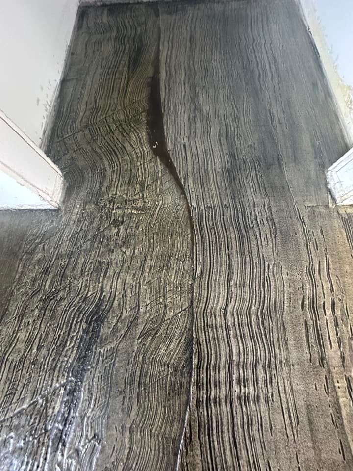 Gray wood-look flooring with a dark, wet-looking streak down the middle, next to a white door frame.