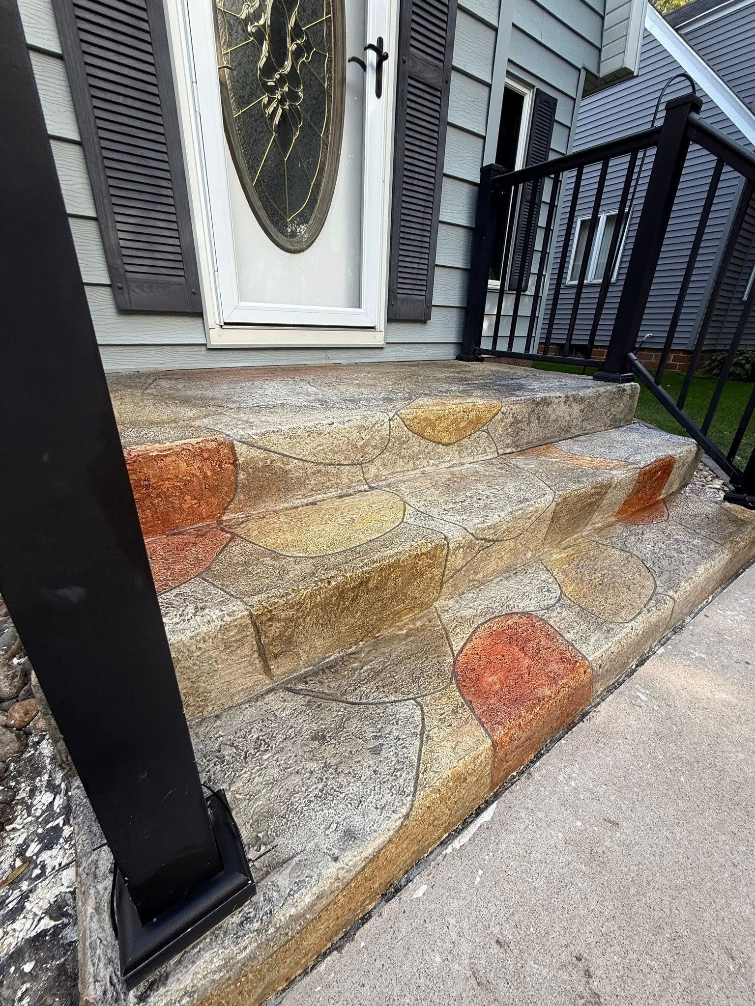 Stone steps leading to a house entrance with a black railing and a decorative front door.