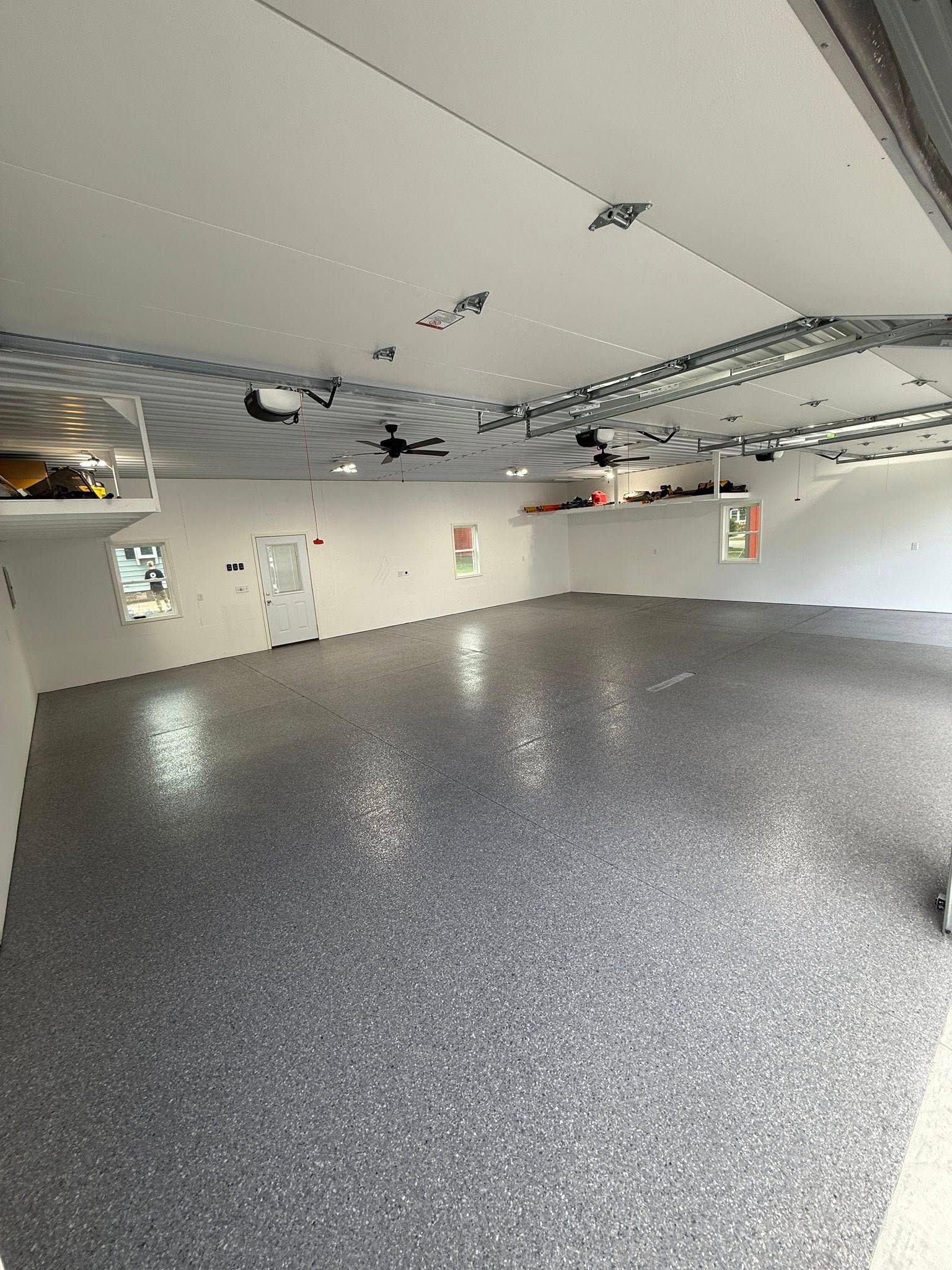 Spacious garage interior with a gray speckled epoxy floor and bright white walls and ceiling.