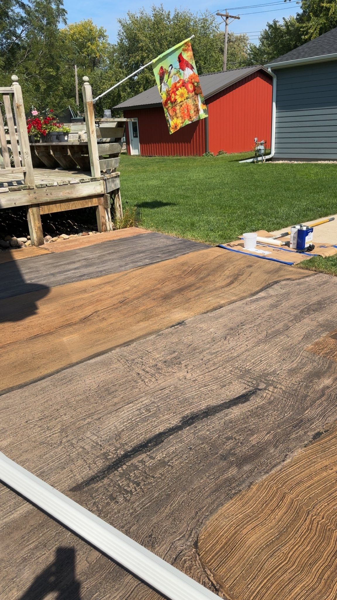 Patio with weathered wooden deck, textured mats in browns and gray, backyard with red shed.