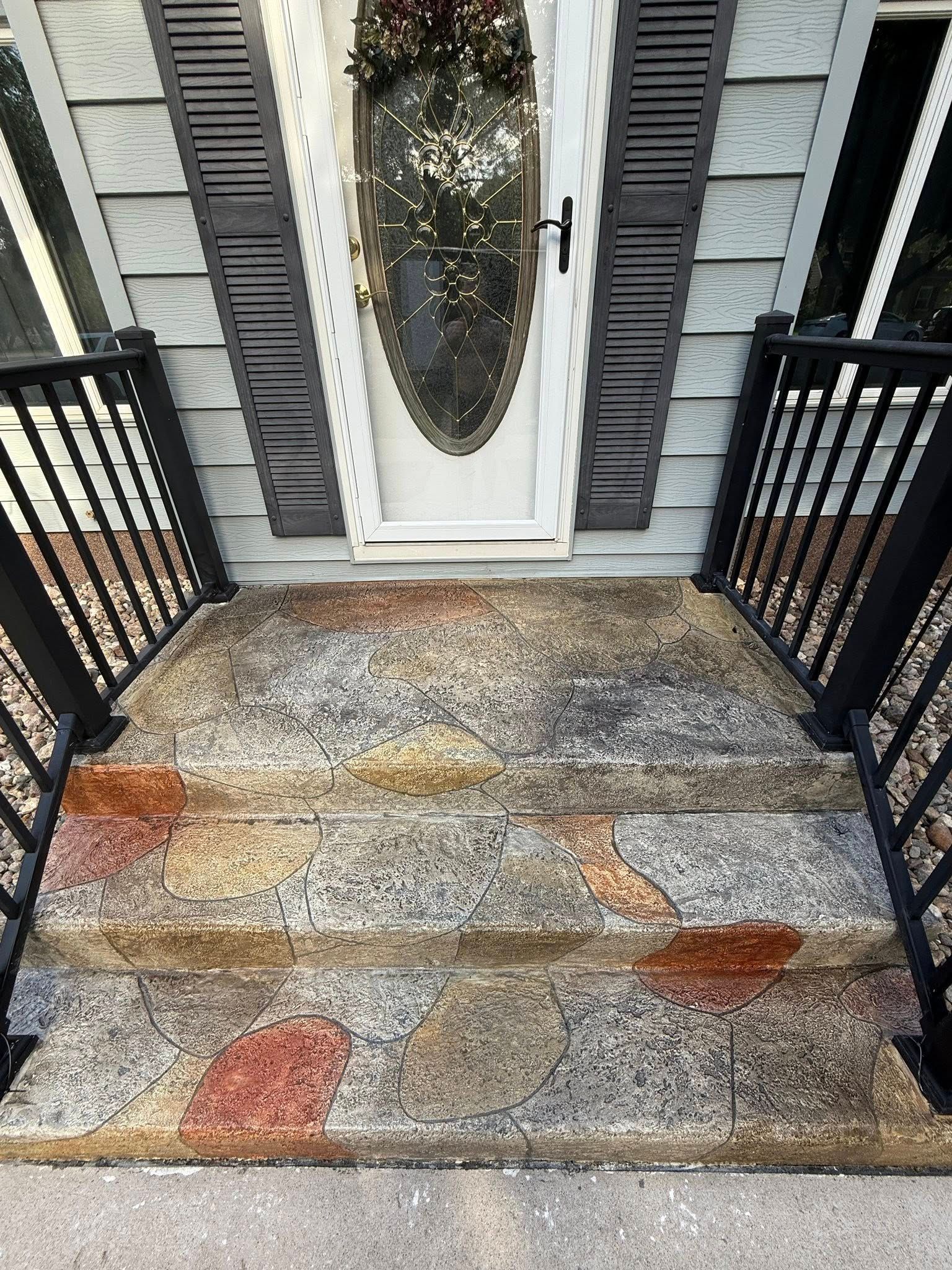 Concrete front steps leading to a front door with decorative stone pattern. Black railings on either side.