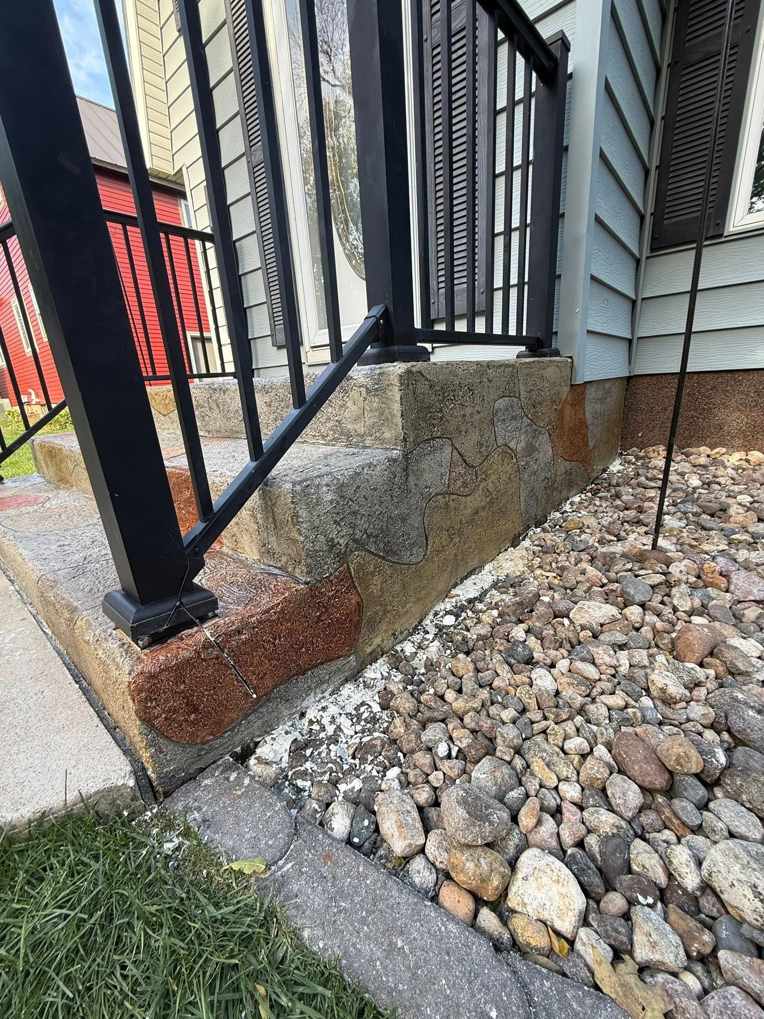 Steps leading to a porch with black railing. The steps are pebble-covered, with a gravel bed.