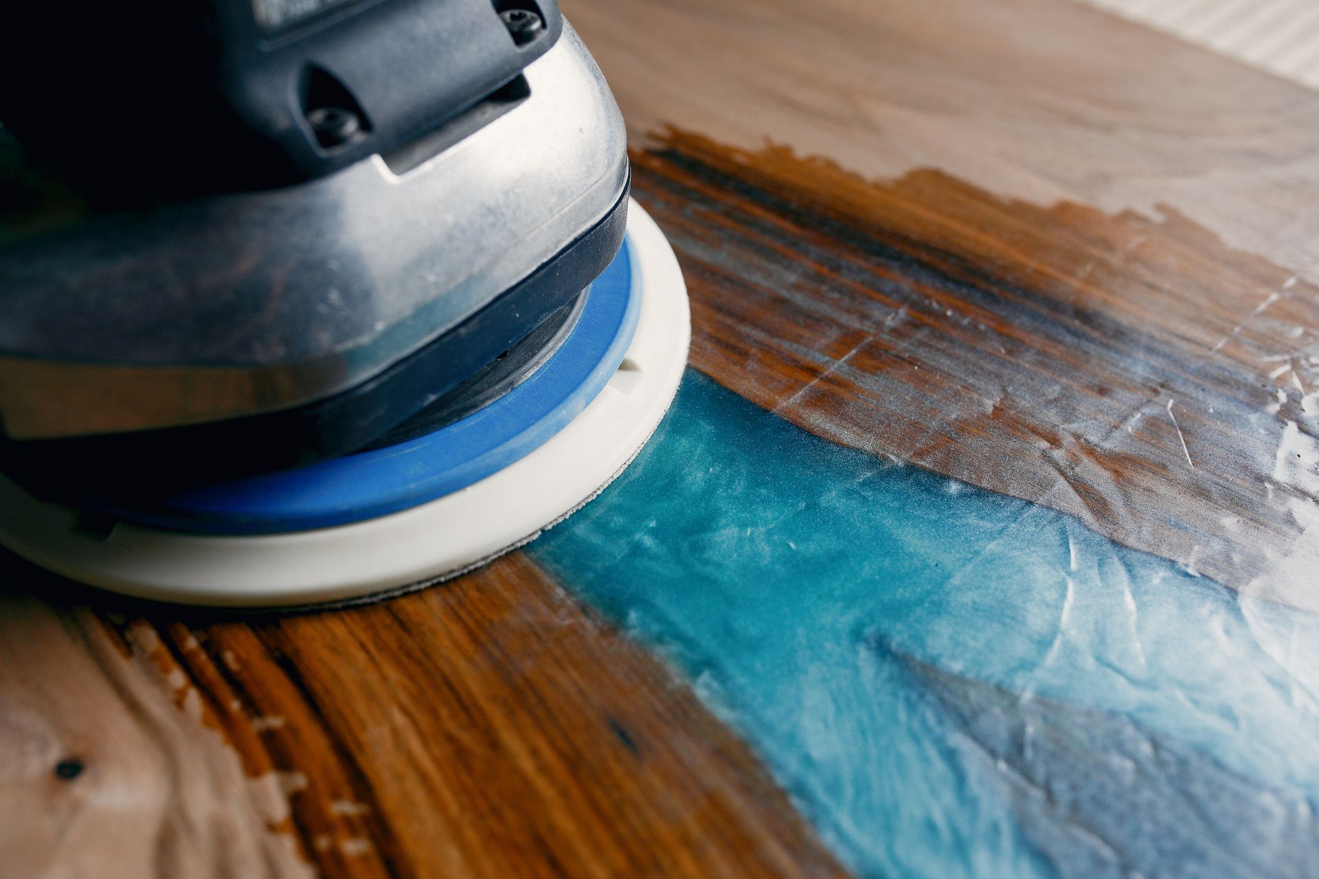 A hardwood floor expert in Port Washington is sanding a piece of wood with a sander.