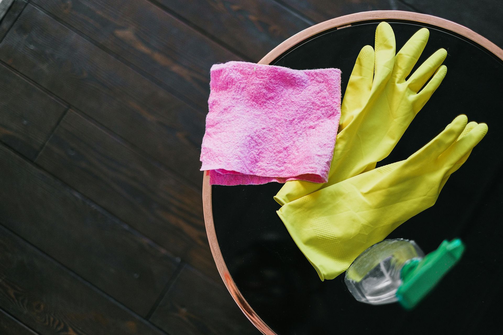 Pink cloth and yellow gloves on a black table with floor cleaning supplies, top-down shot.