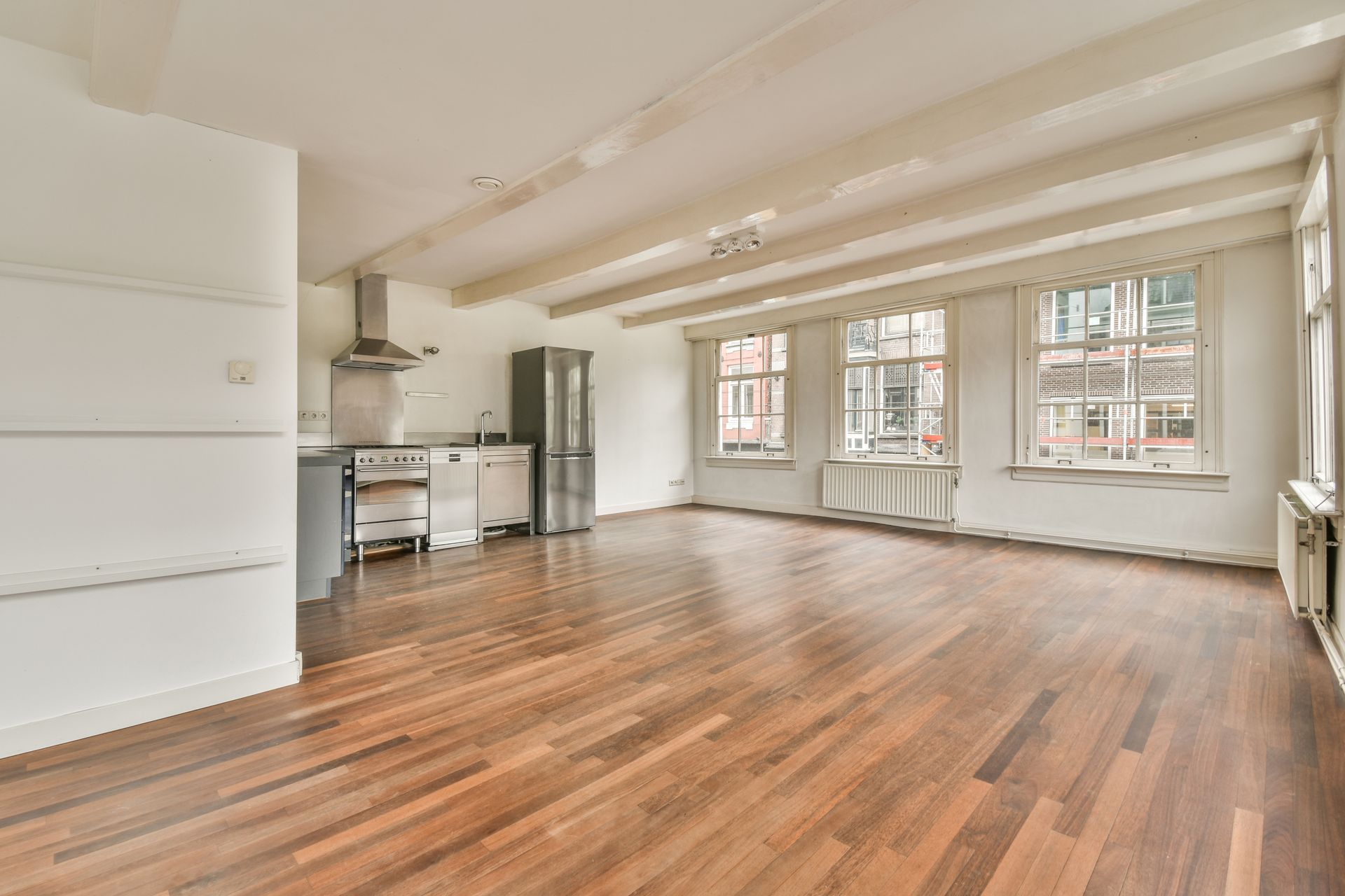A large empty room with hardwood floors and a kitchen.