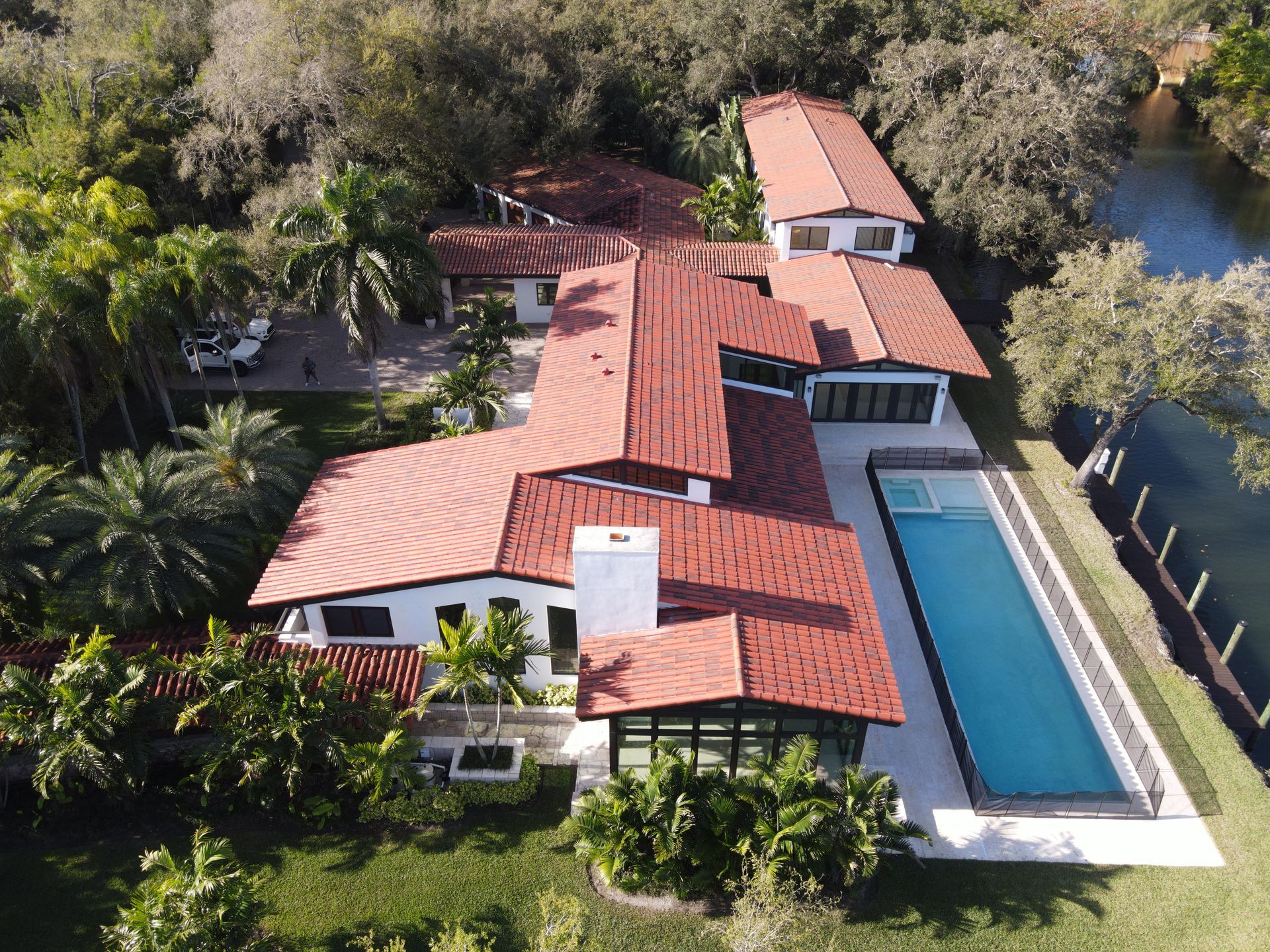 Aerial view of a white stucco house with a red tile roof and a long pool next to a waterway.
