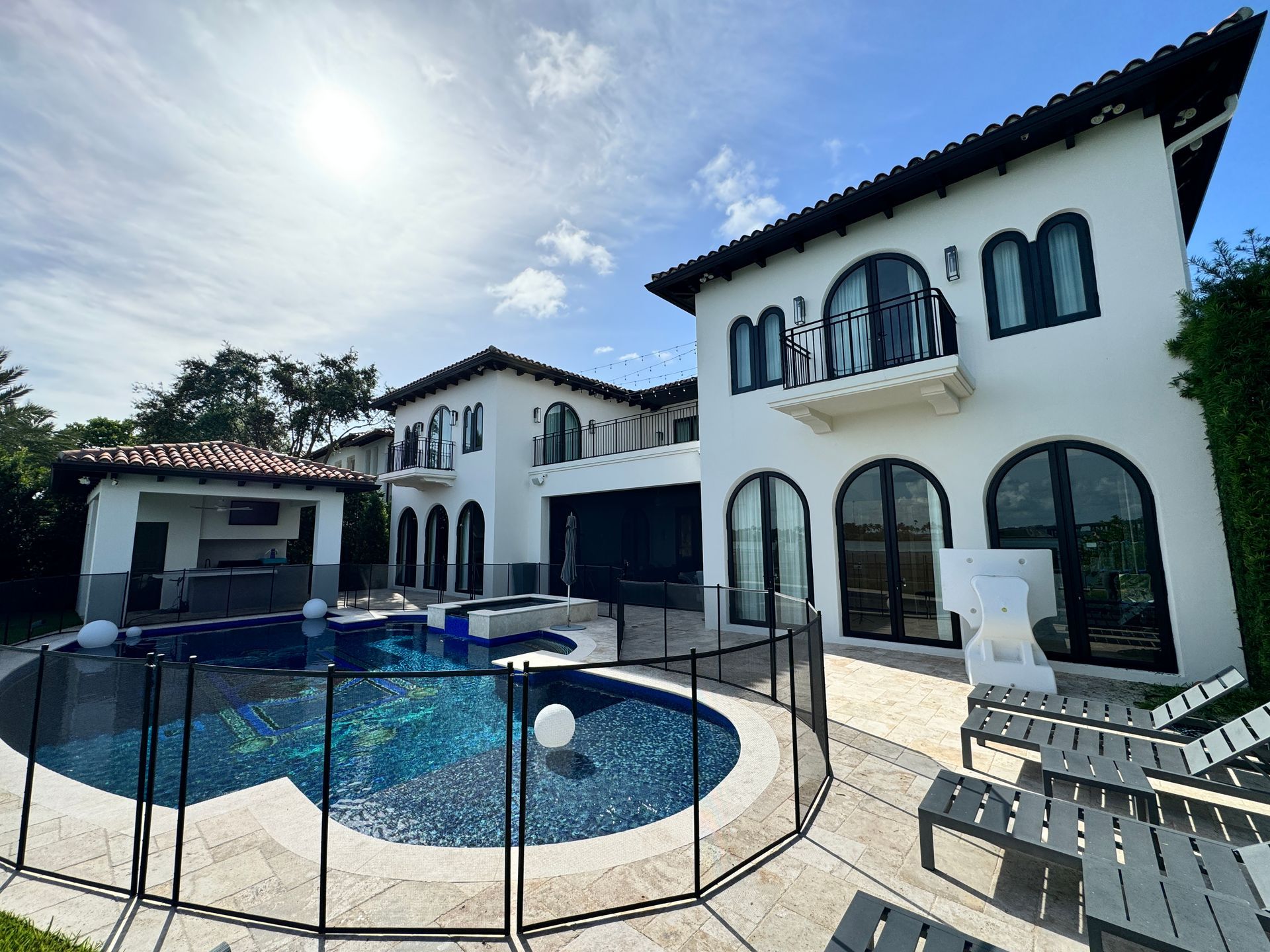 Luxury white house with pool, black trim, and outdoor lounge area. Sunny day.