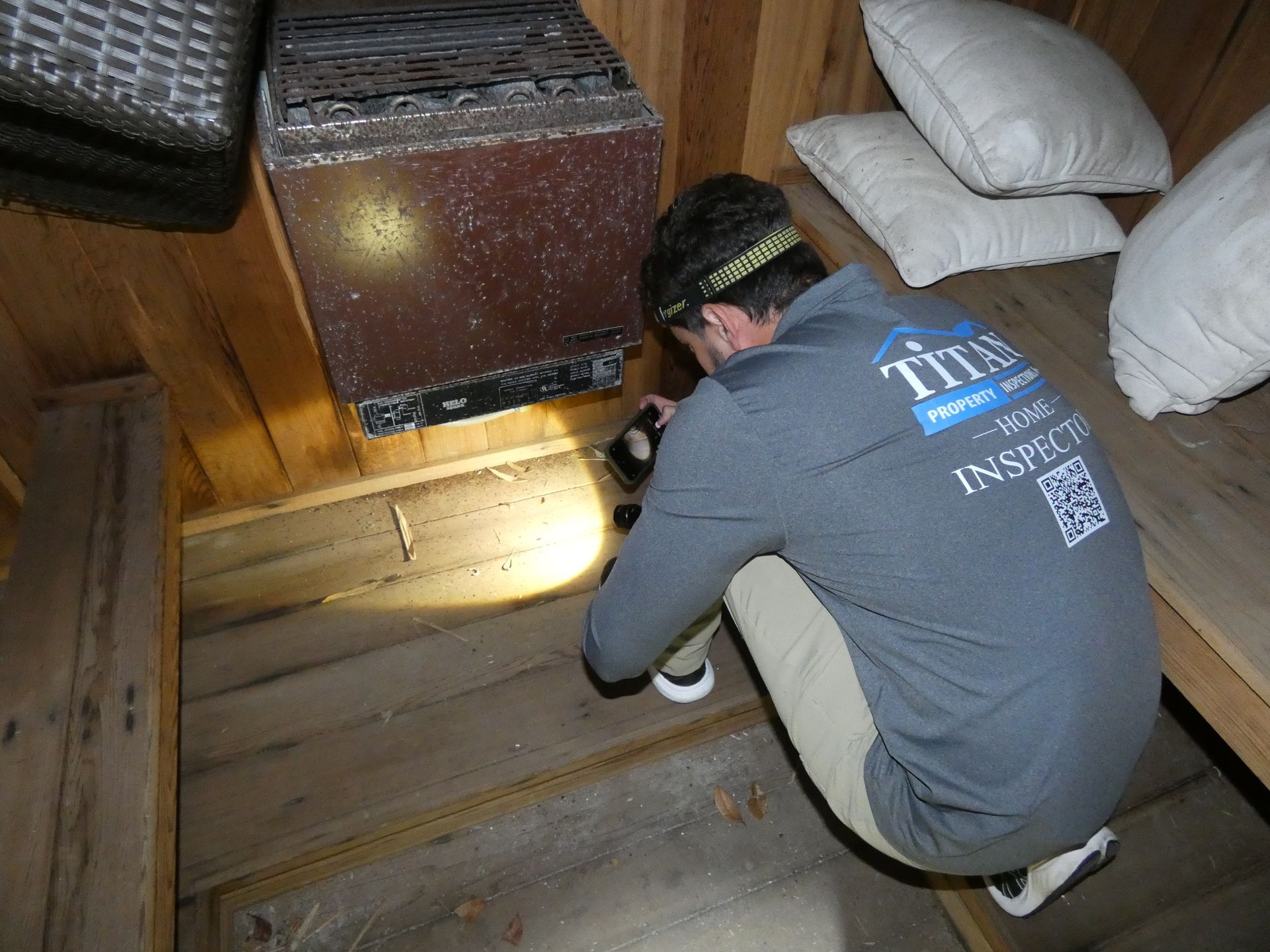 Man inspecting sauna interior with a flashlight. Wooden benches, heater, and pillows visible.