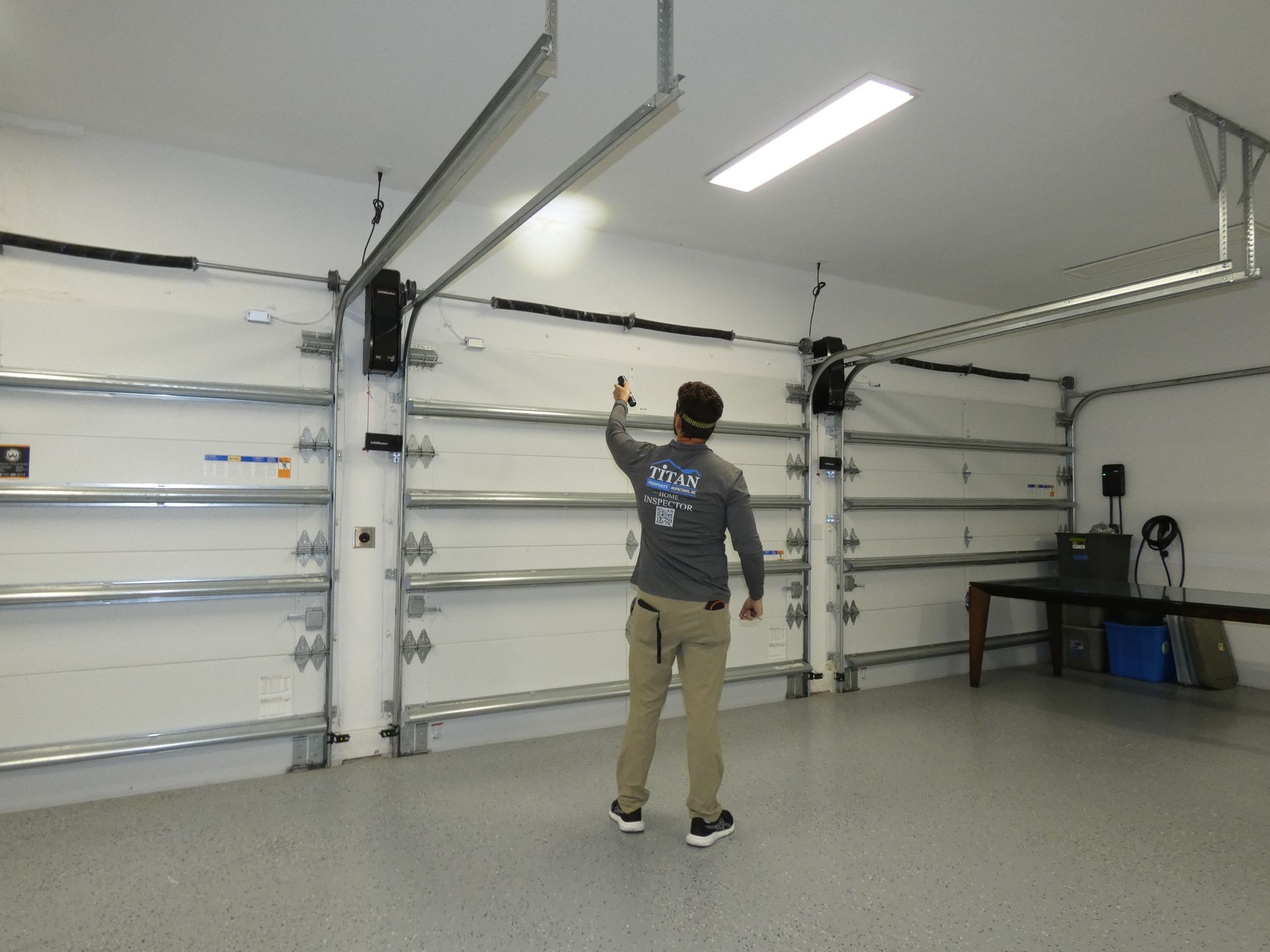 Person in a garage pointing upwards, near a garage door. The garage has white walls and a gray floor.