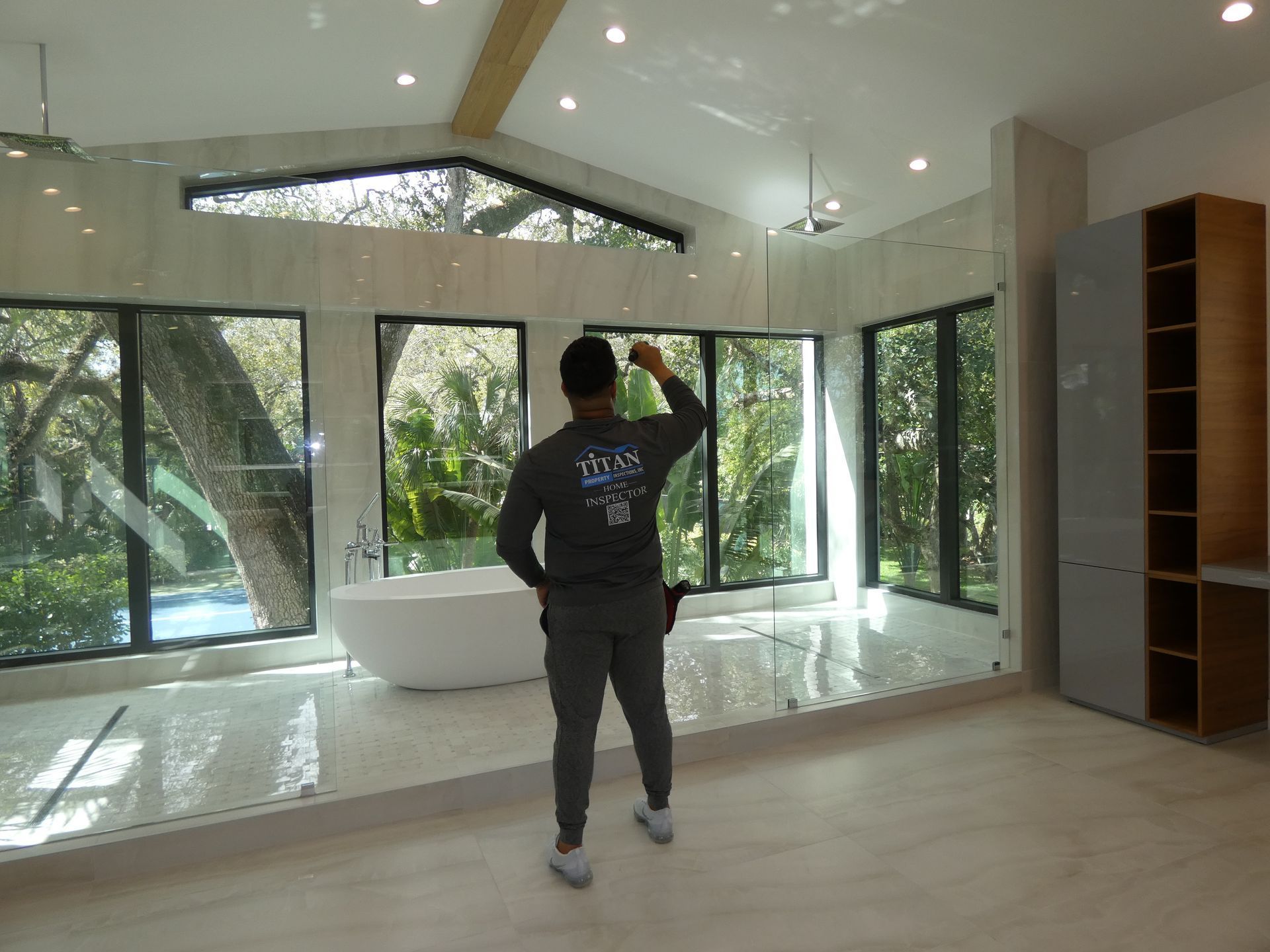Man in a bathroom with large windows, gesturing toward the ceiling. A bathtub is visible.