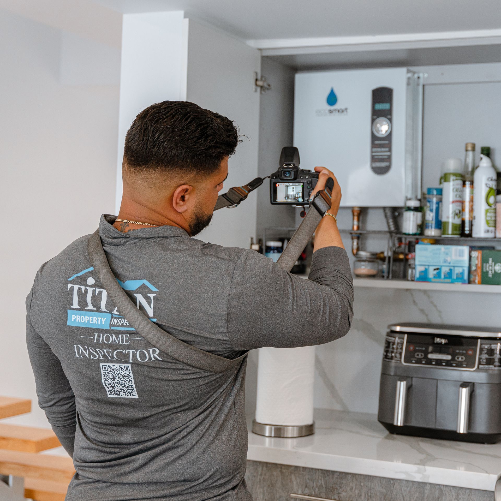 Home inspector takes photo of water heater inside kitchen cabinet.