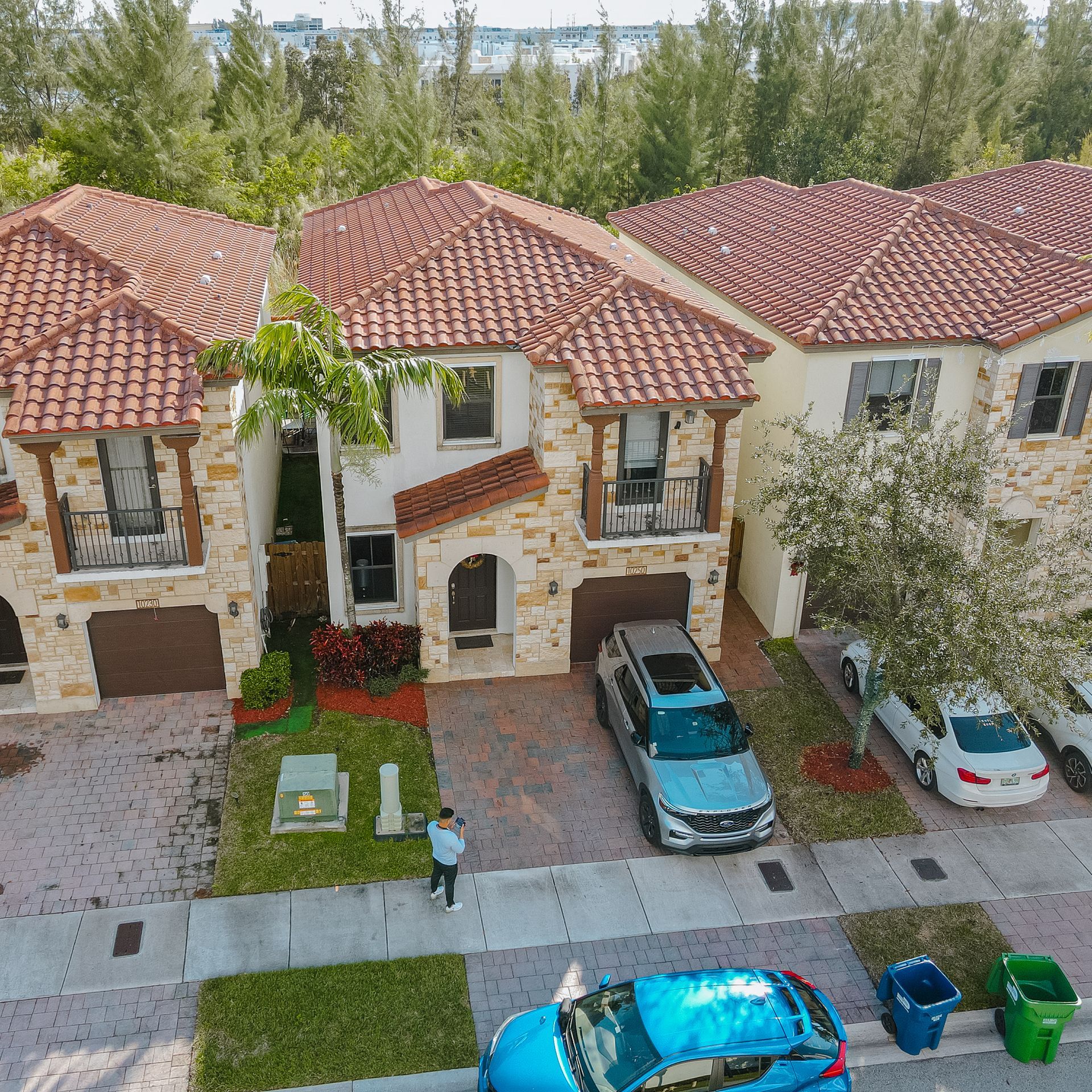 Row of townhouses with red tile roofs, beige stone facade, and parked cars on the street.