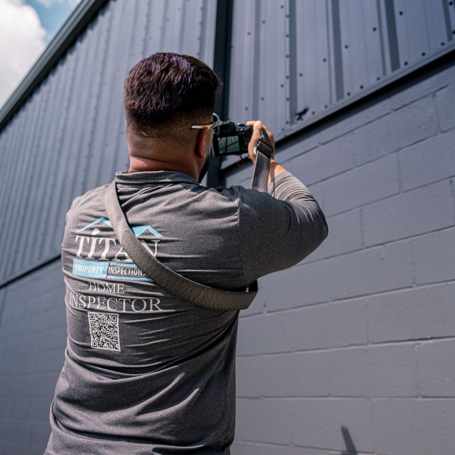 Person wearing shirt with company logo, taking photo of a gray building.