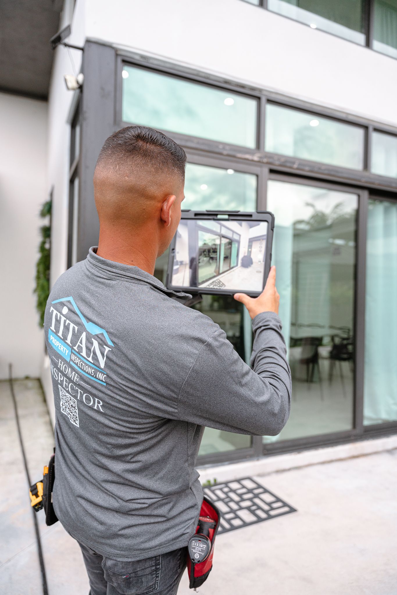 Man using a tablet in front of a building with sliding glass doors; Titan logo on shirt.