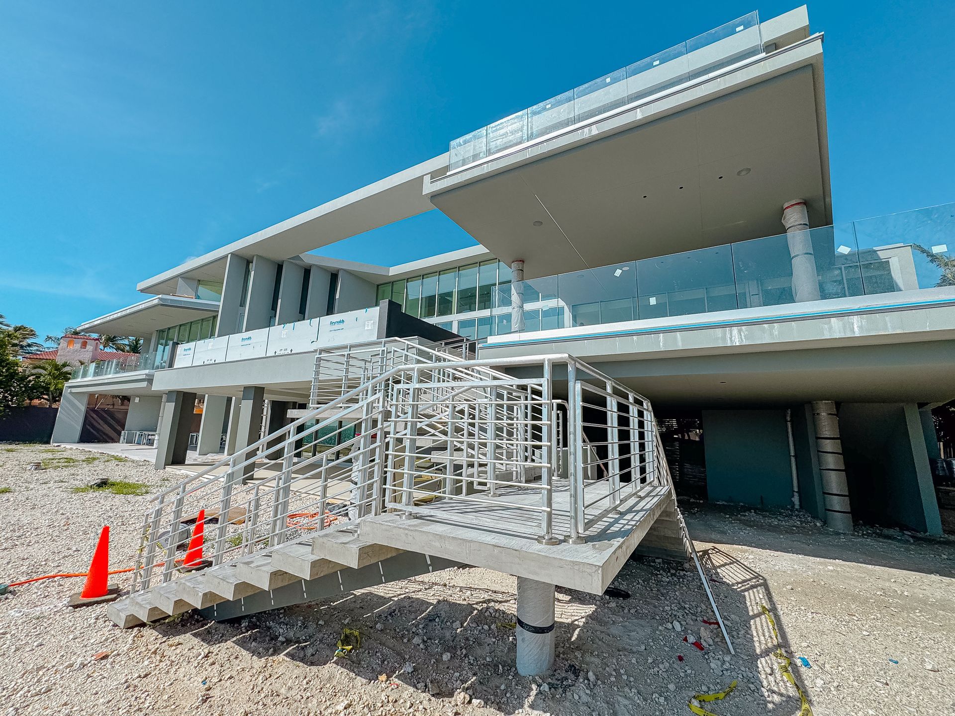 Modern building under construction with glass railings, stairs, and concrete supports on a bright day.