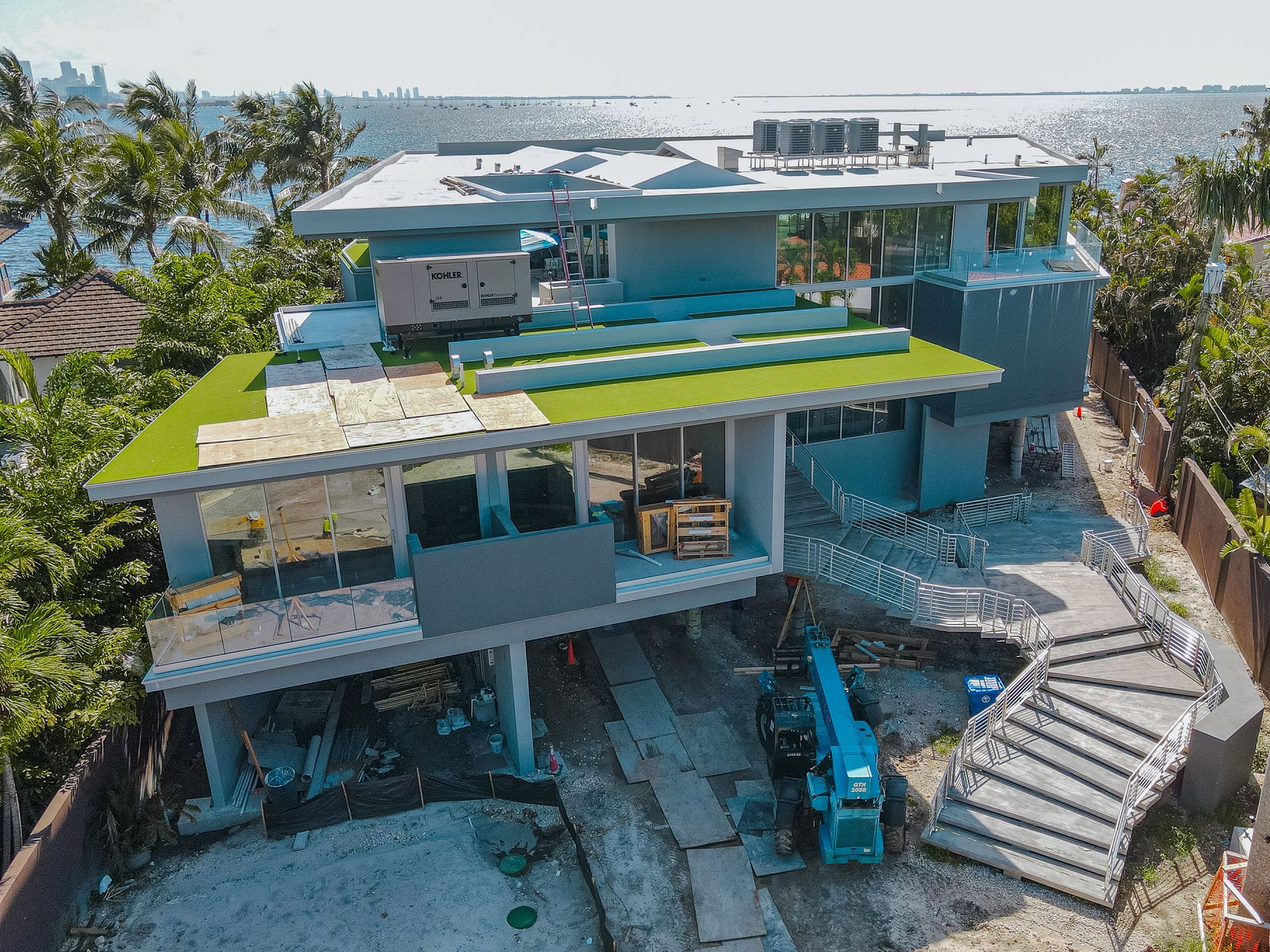 Modern multi-level house under construction with partial green roof; ocean in background.