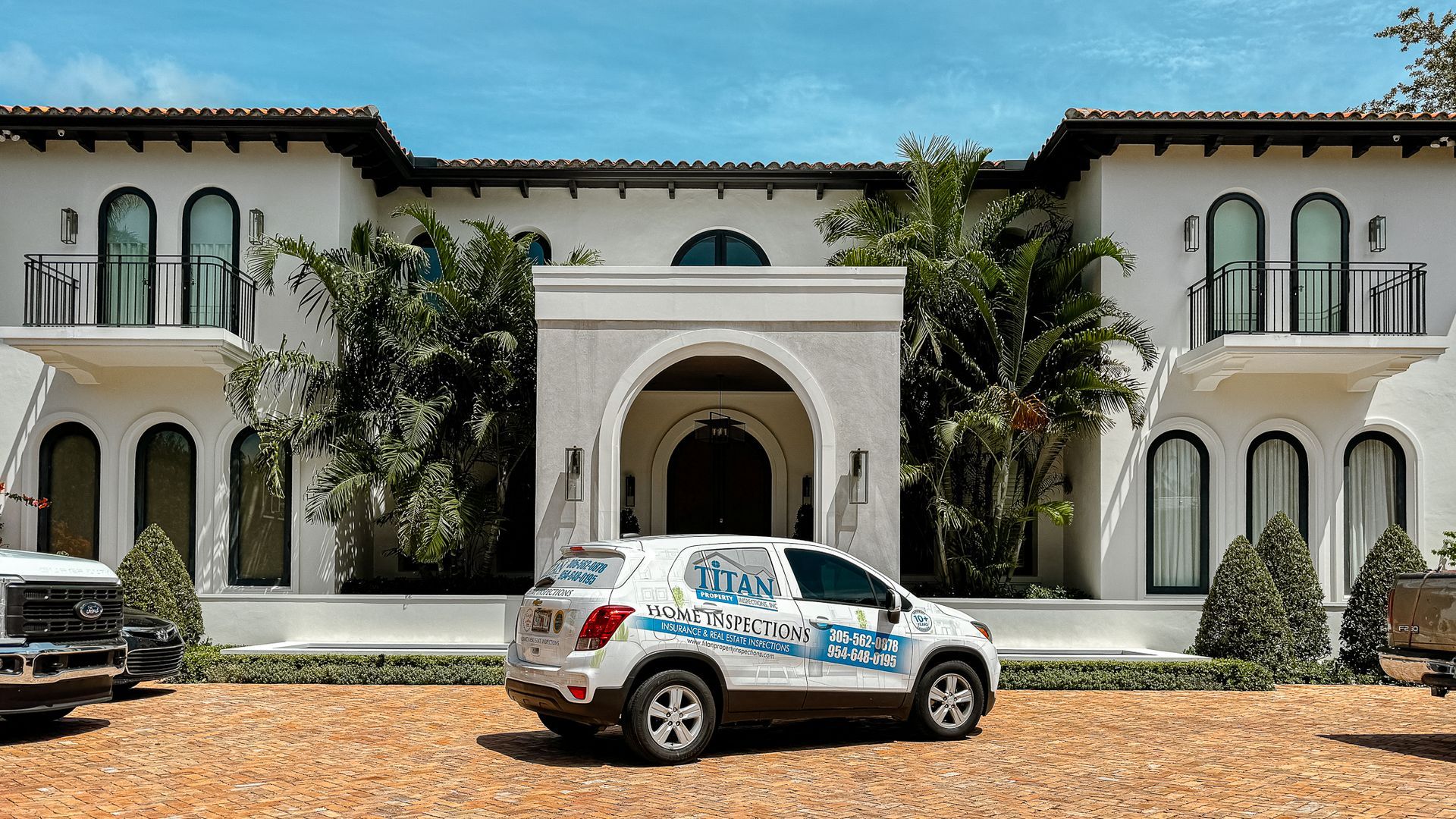 White SUV with business logo parked in front of a white mansion with palm trees.