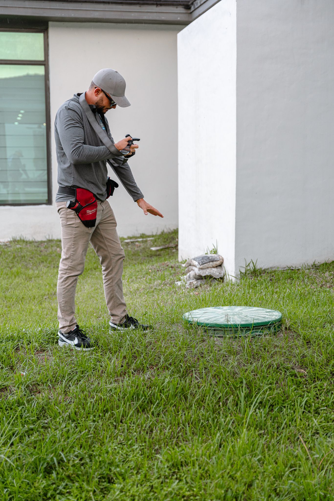 Man inspecting a green utility cover on a lawn near a building.