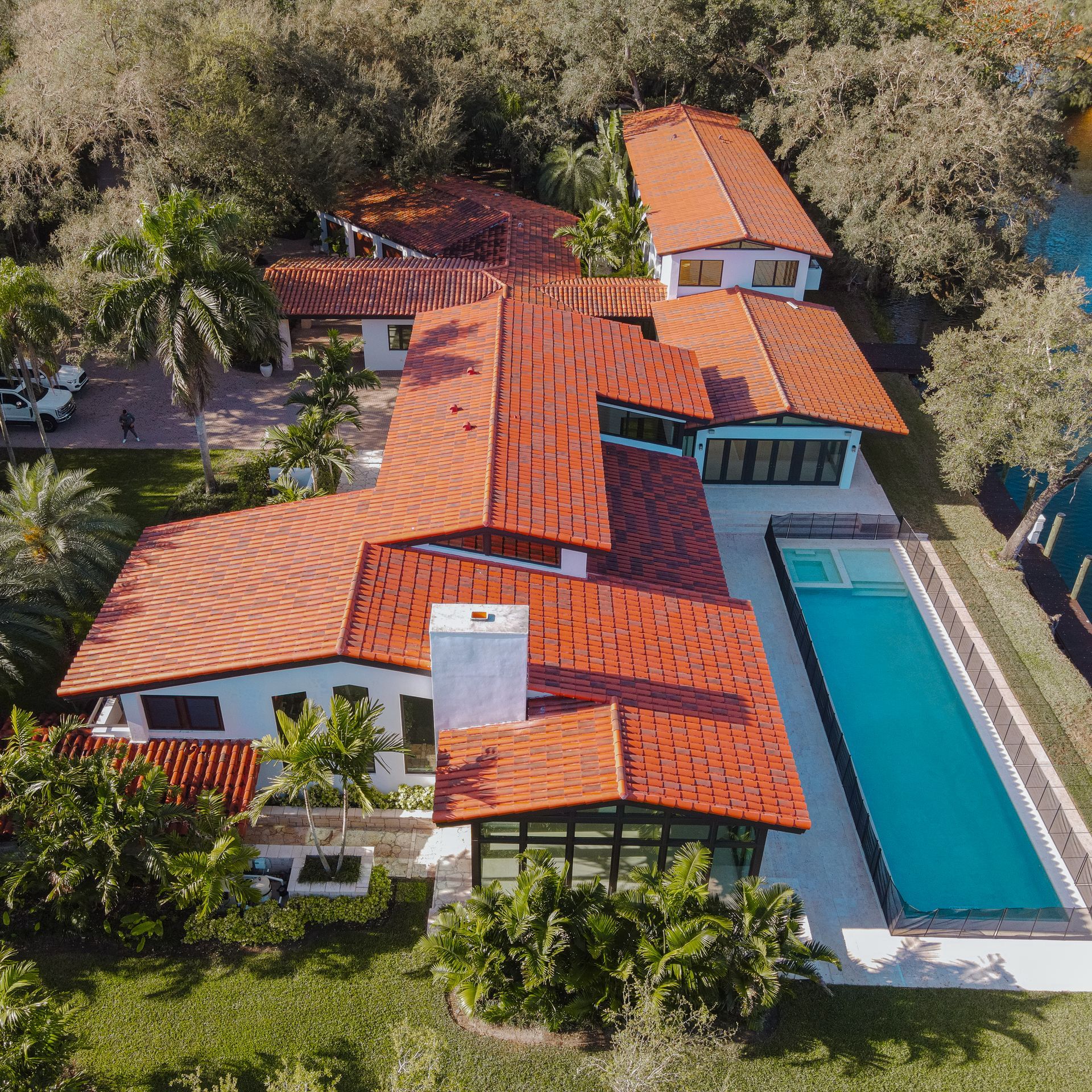 Aerial view of a large white house with a red tile roof and a long rectangular pool.