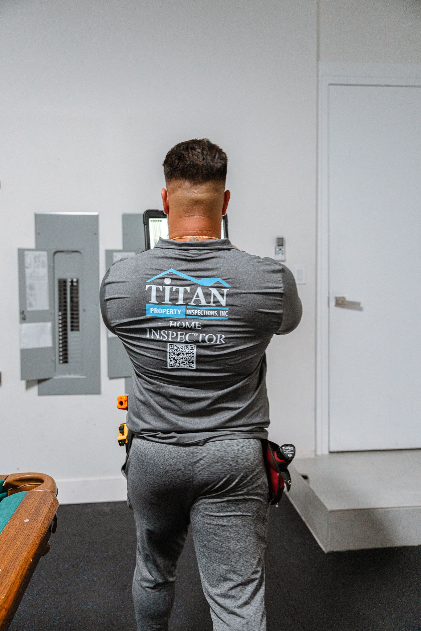 Man in grey shirt and pants standing in front of electrical panel, arms crossed.