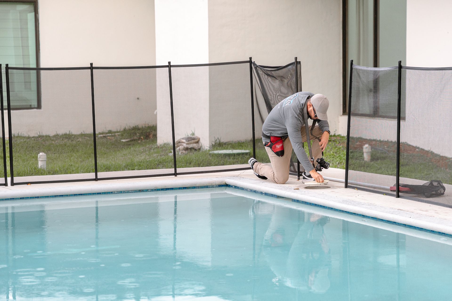 Person kneeling near a pool installing a black mesh safety fence around the water.