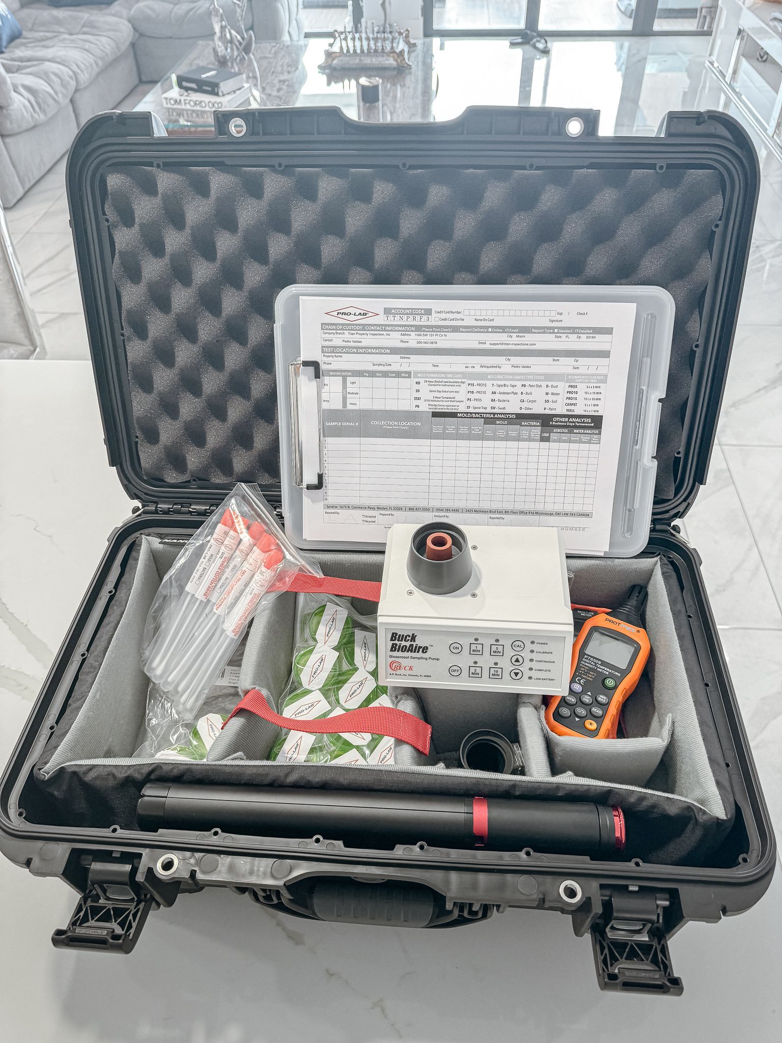 Black case open, containing surveying equipment, paperwork, and an orange handheld device, on a reflective surface.