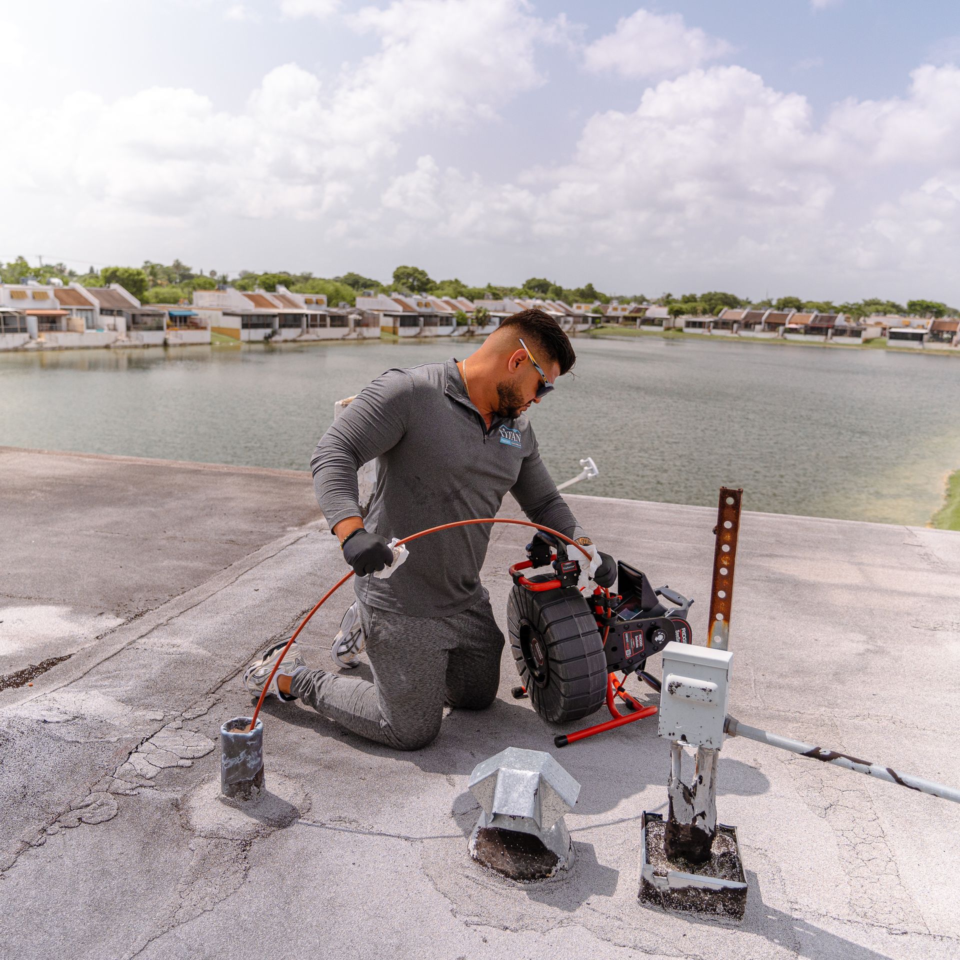 A person on a rooftop, using equipment to inspect plumbing near a body of water.