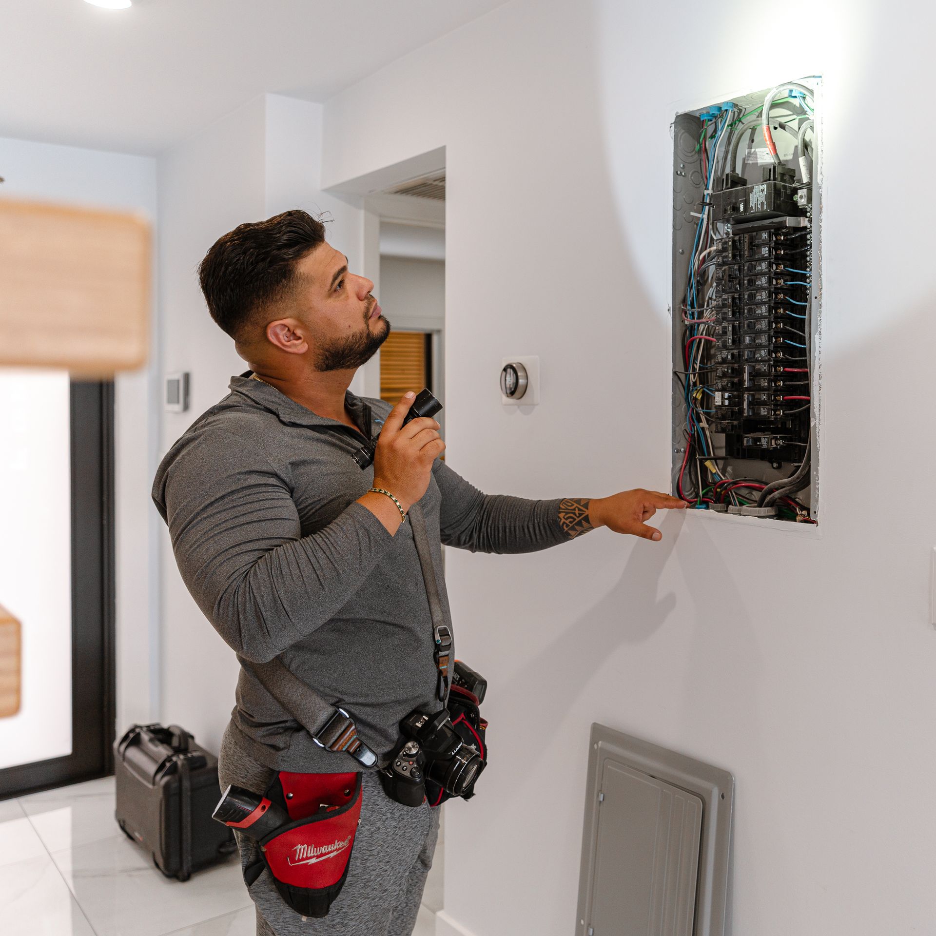 Electrician examining a circuit breaker panel with a flashlight in a hallway.