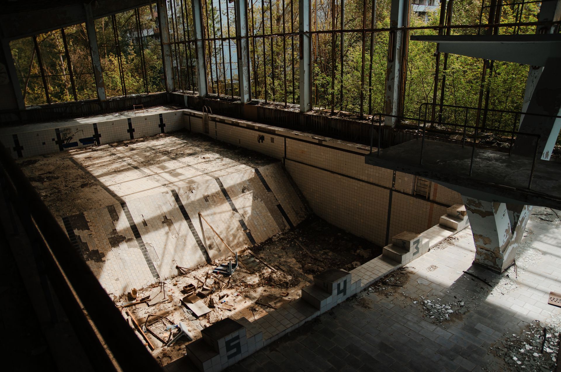 An abandoned swimming pool with peeling paint and debris, overgrown with vegetation.