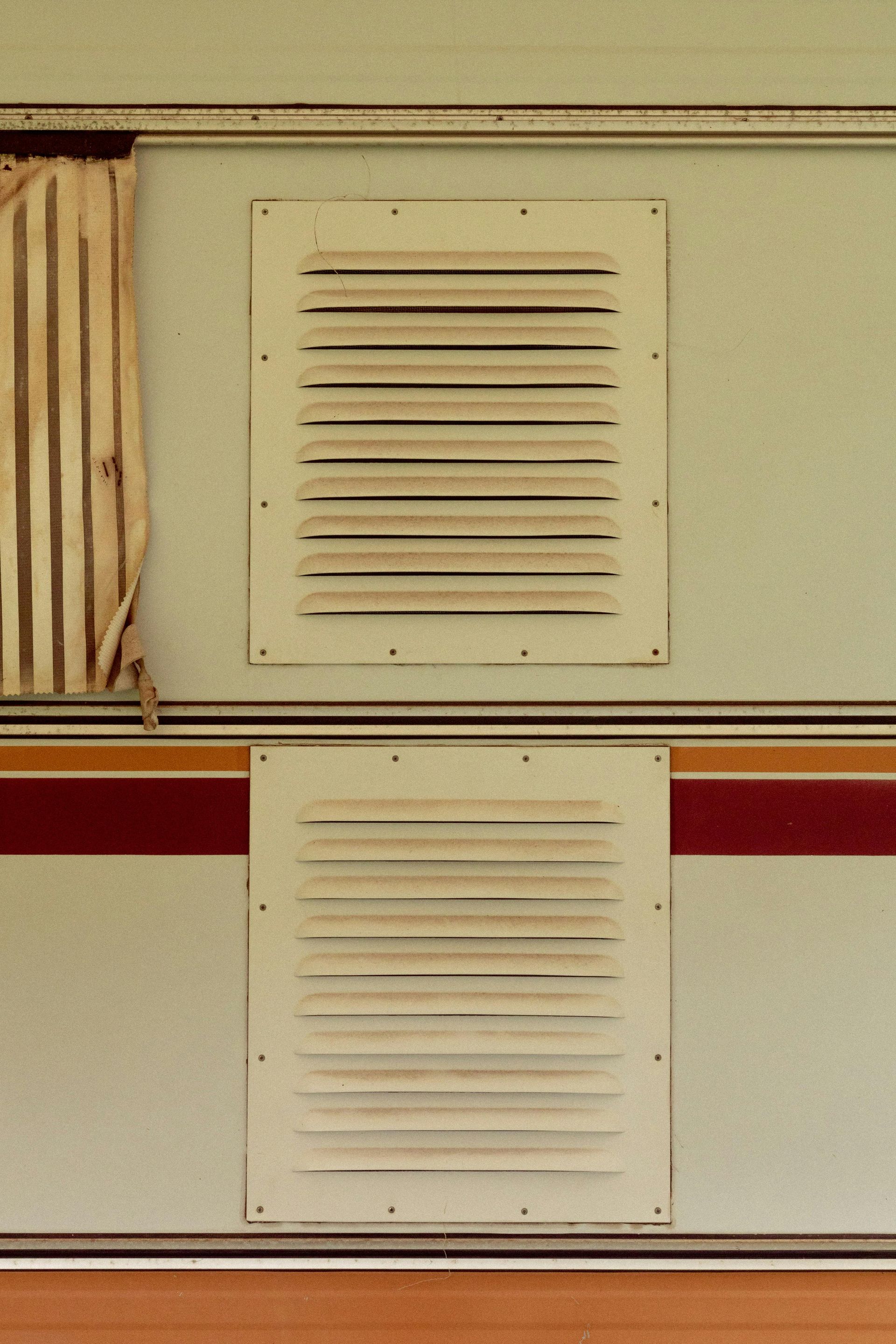 Two white rectangular air vents on the side of a camper, above and below a red and brown stripe.