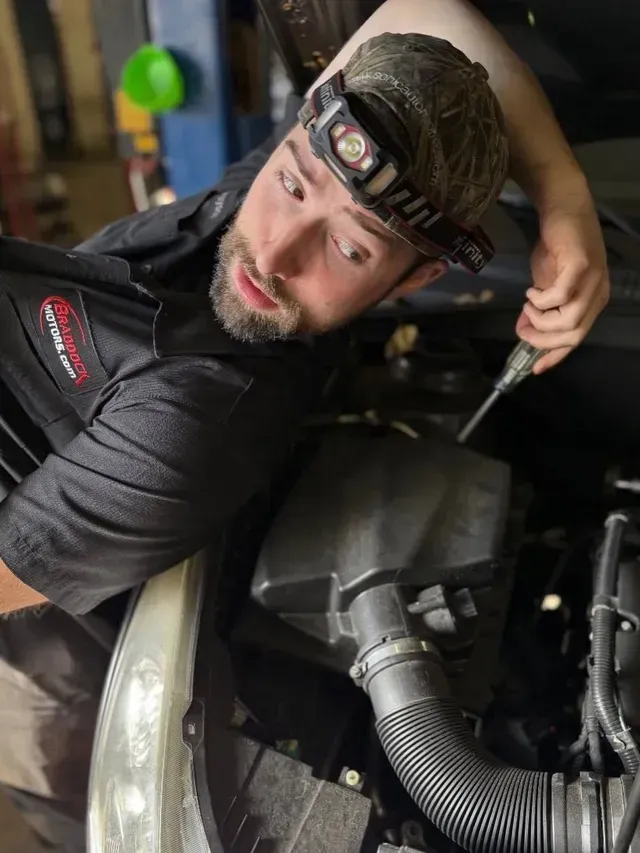 Mechanic leaning over an engine bay, wearing a headlamp and working with tools | Braddock Motors Service
