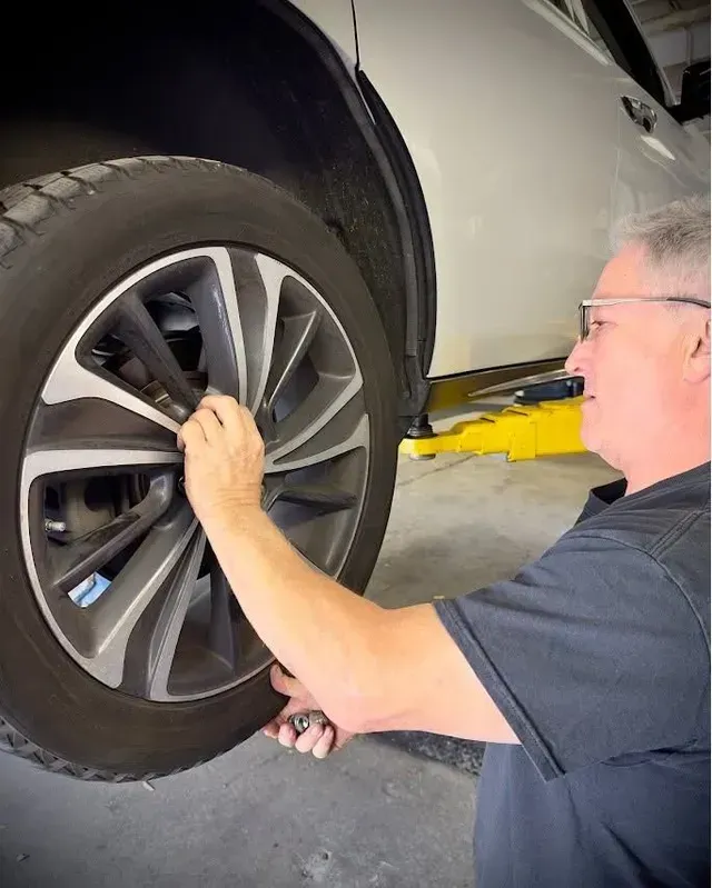 Mechanic inspecting a car wheel at a garage lift | Braddock Motors Service