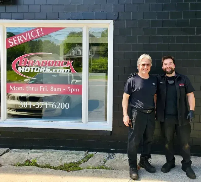 Two mechanics standing outside a garage with a Braddock Motors service sign in the window | Braddock Motors Service