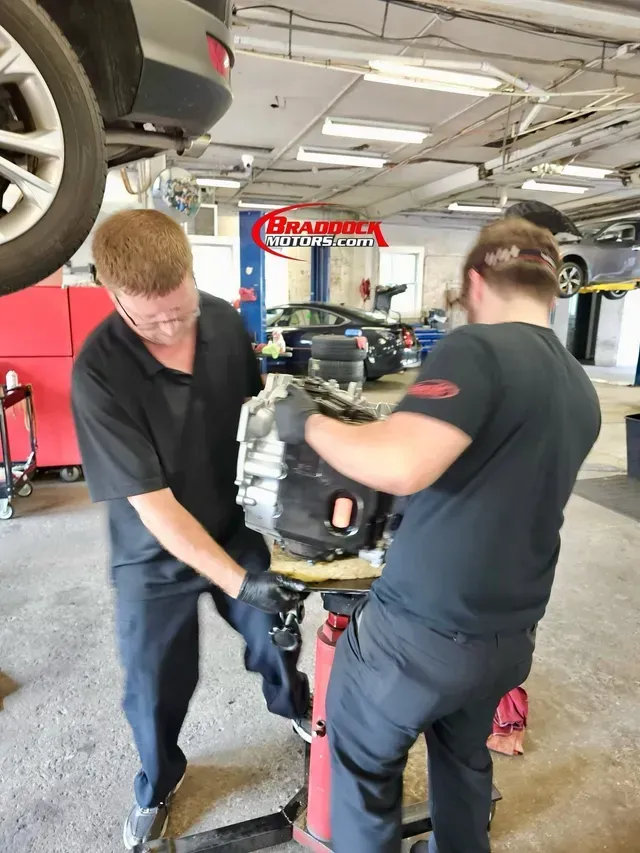 Two mechanics adjusting an engine on a stand in an auto repair shop | Braddock Motors Service