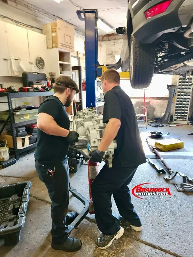Two mechanics in a garage inspecting a car lifted on a hoist | Braddock Motors Service