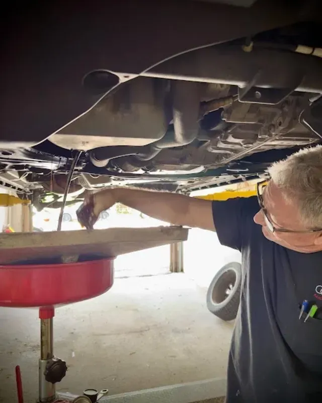 Mechanic draining fluid from a car into a red catch pan underneath the vehicle | Braddock Motors Service