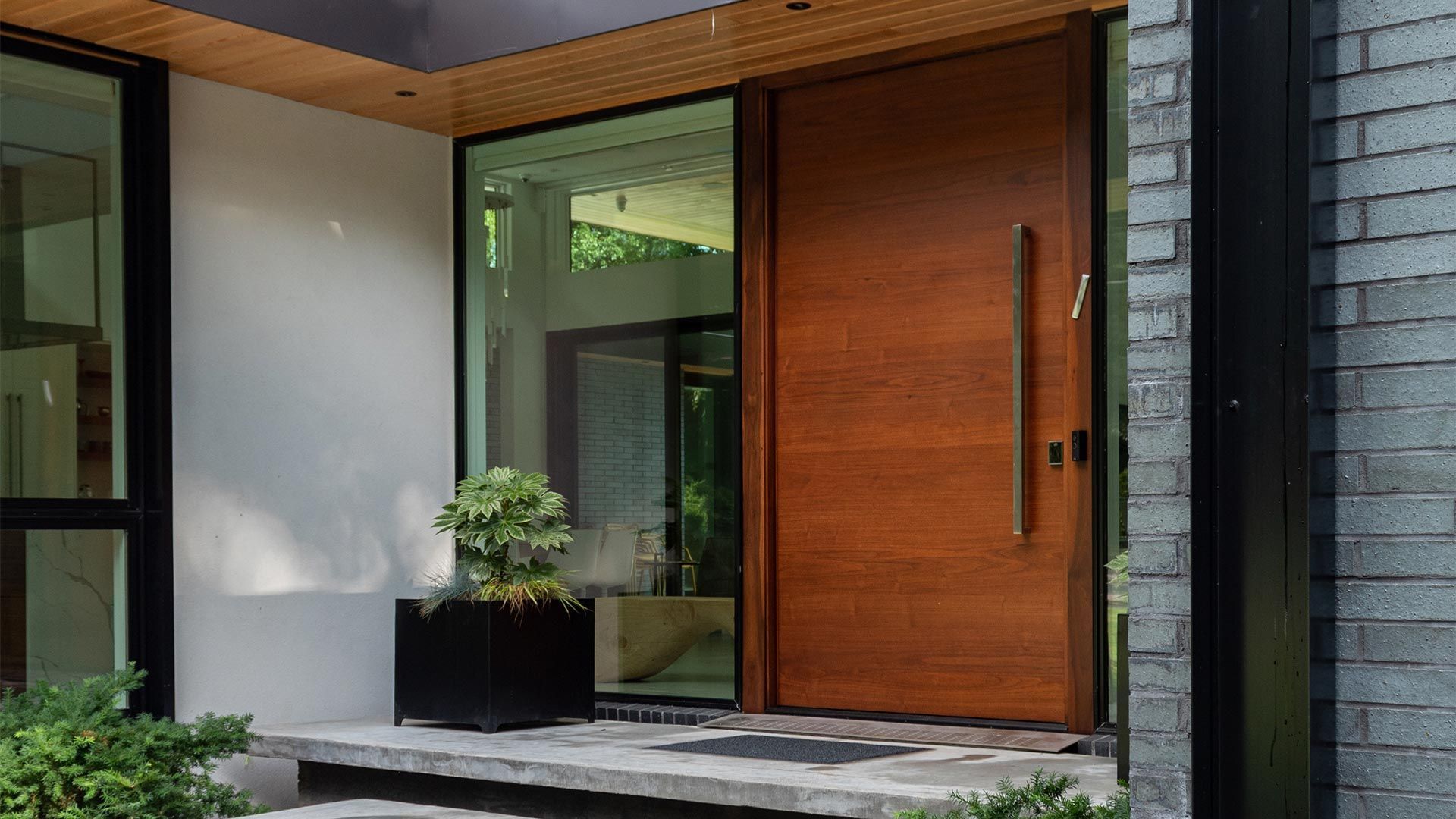 Modern house entrance with a wooden front door, stone steps, and potted plants under a covered porch